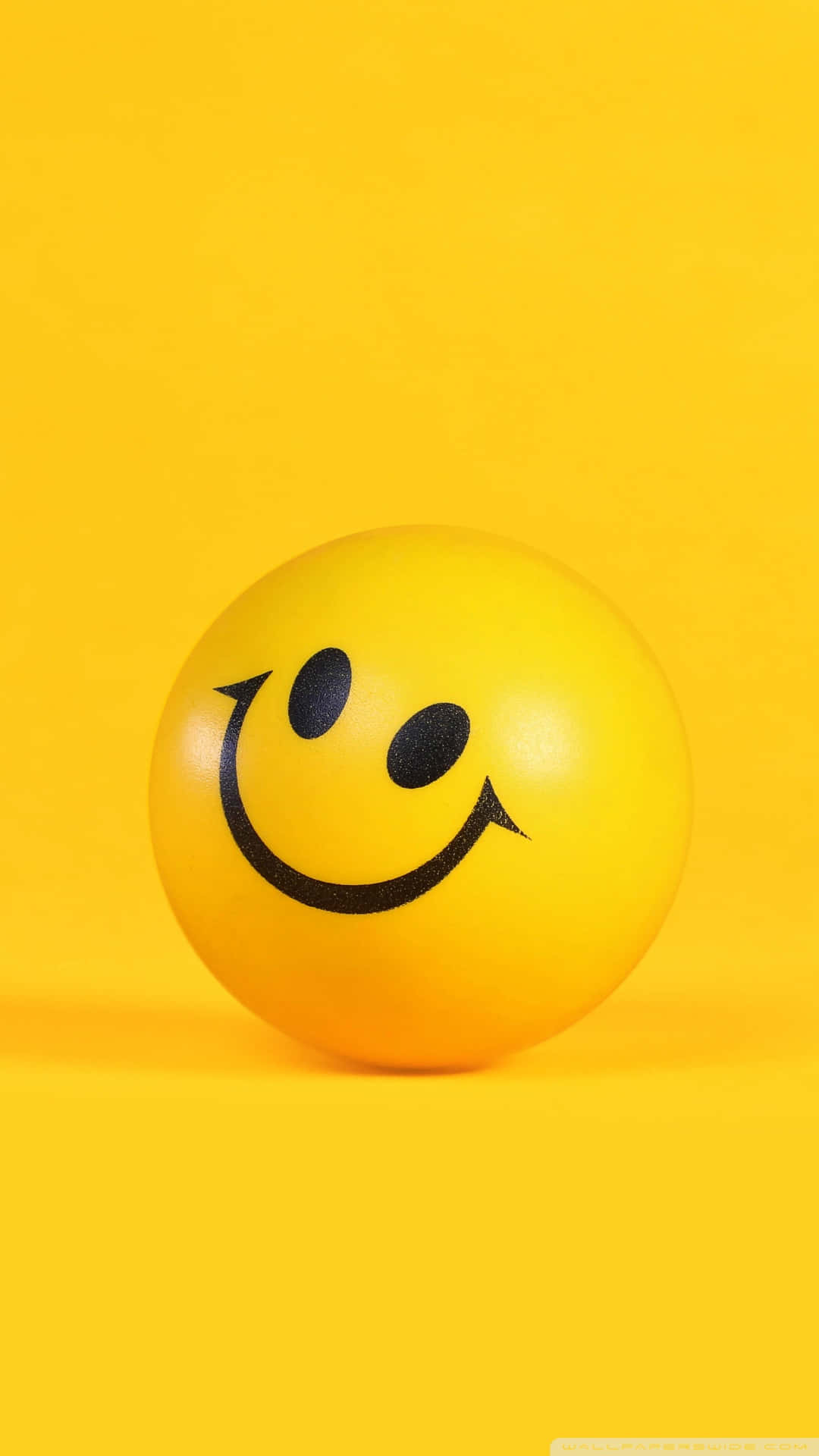Aesthetic Smiley Face 桌布 壁紙 — 一個明亮的黃色笑臉球放在純黃色背景上，投射出柔和的陰影。