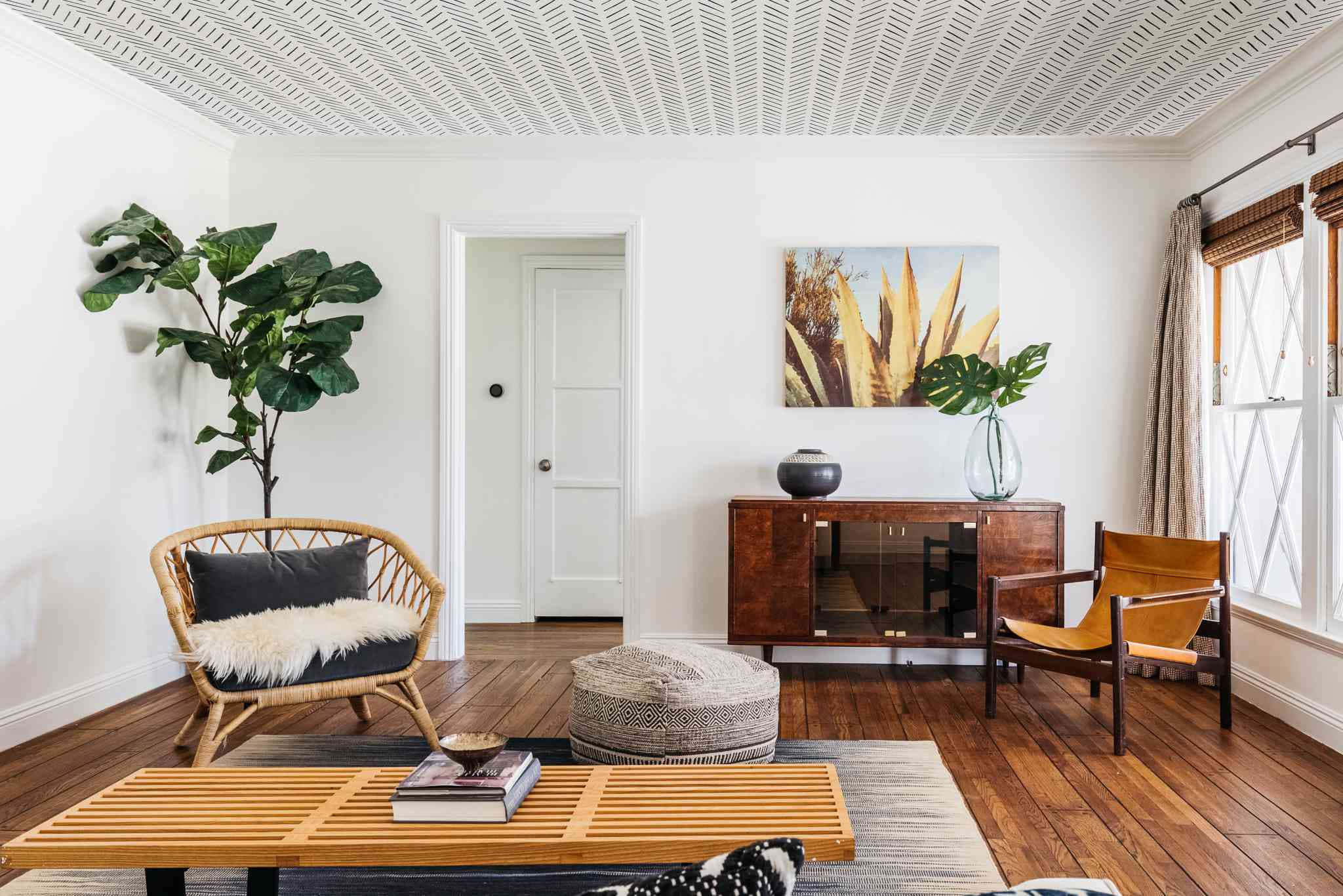 Interior Design 桌布 壁紙 — 一個明亮通風的客廳，配有木地板、藤椅和一棵大琴葉榕，位於白色方格天花板下。