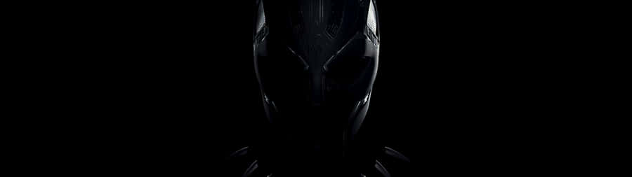 Marvel Black And White 桌布 壁紙 — 一個昏暗照明的黑豹面具在漆黑背景中微微發光，突顯其複雜的設計和威嚴的輪廓。