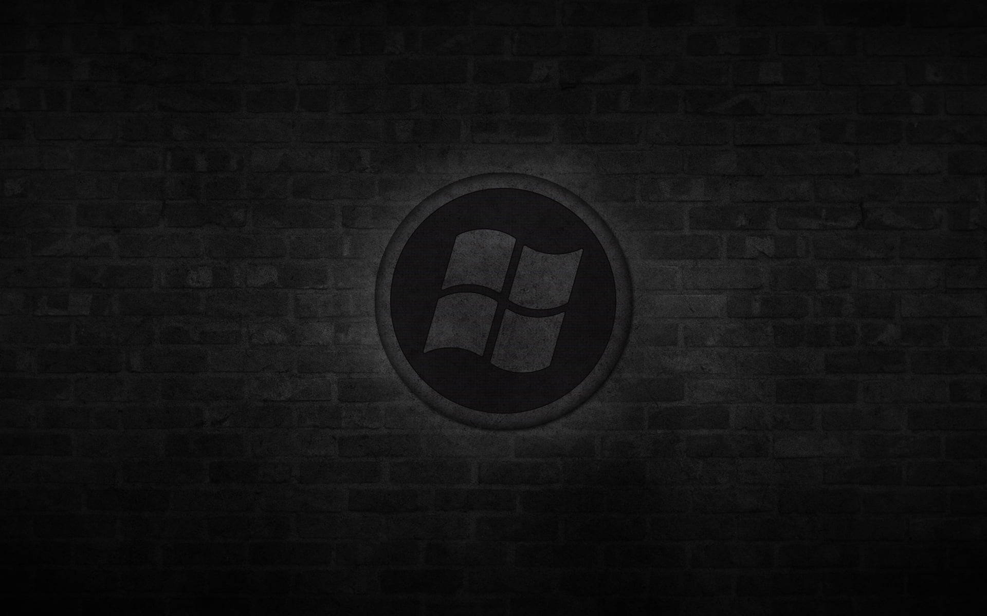 Brick Wall 桌布 壁紙 — 一個昏暗的Windows標誌嵌入在深色磚牆中，帶有微妙的聚光燈照明。