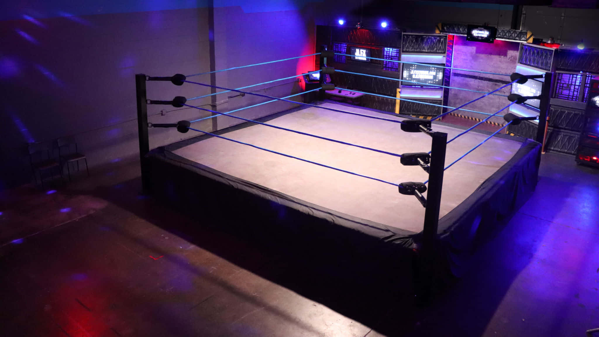 Wrestling Ring 桌布 壁紙 — 一個昏暗的摔角擂台，沐浴在紫色和紅色的舞台燈光中，空蕩蕩的繩索和昏暗的競技場地板。