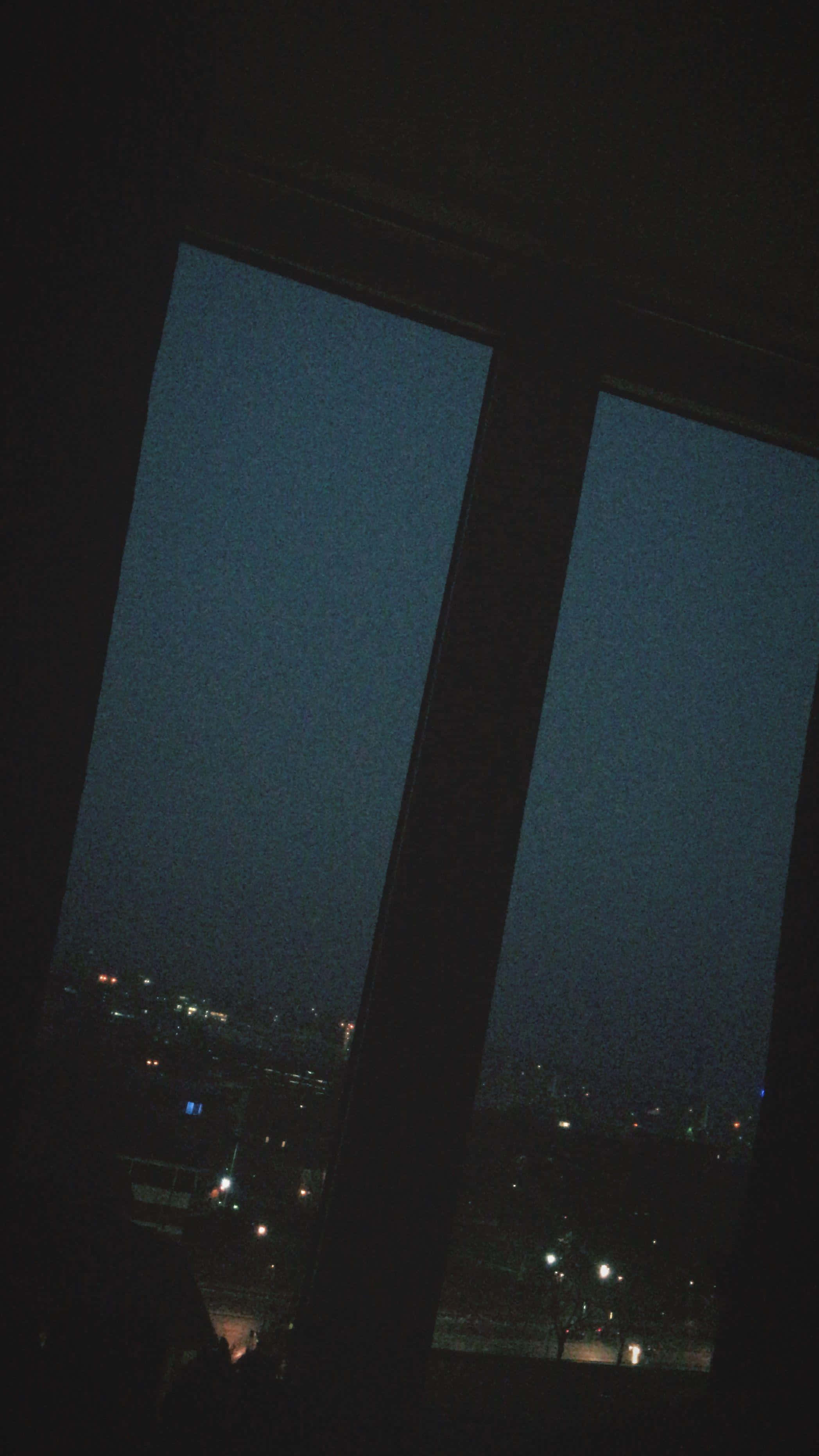 Night Time 桌布 壁紙 — 一個昏暗的窗框捕捉到在深邃暮色天空下，散落燈光閃爍的城市景觀。