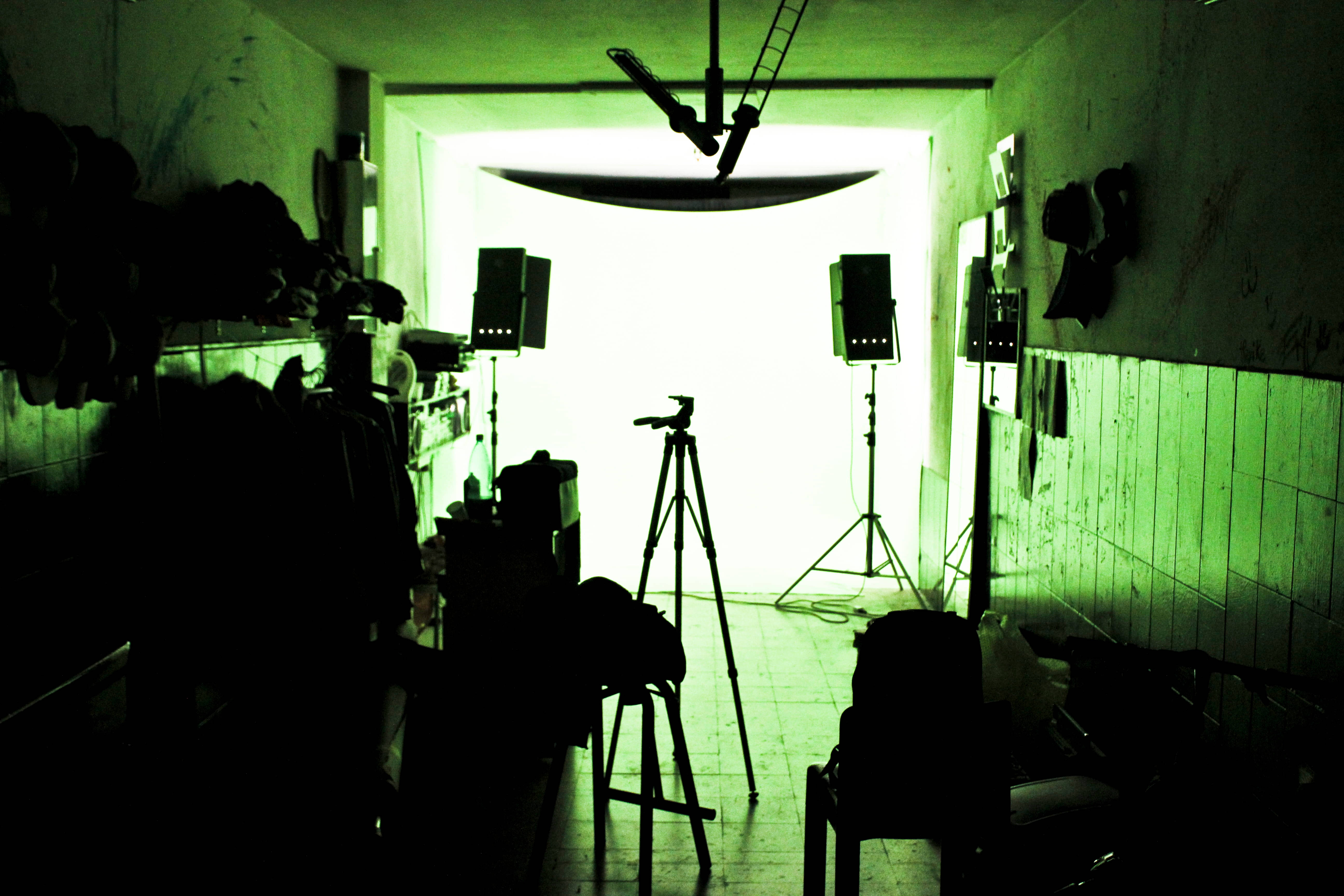 Studio 桌布 壁紙 — 一個昏暗的綠色照明房間，帶有剪影的攝影設備面向明亮的門口。