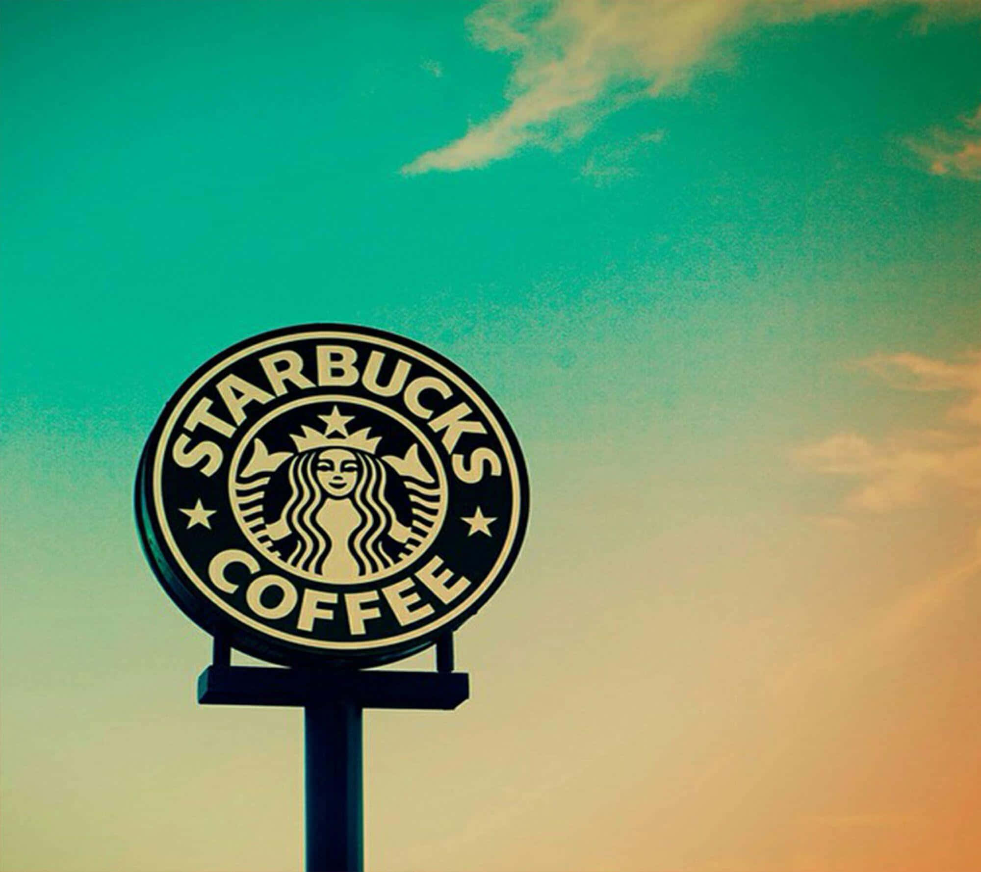 Aesthetic Starbucks 桌布 壁紙 — 一個星巴克咖啡招牌聳立在充滿活力的青綠色和橙色日落天空與薄雲之間。