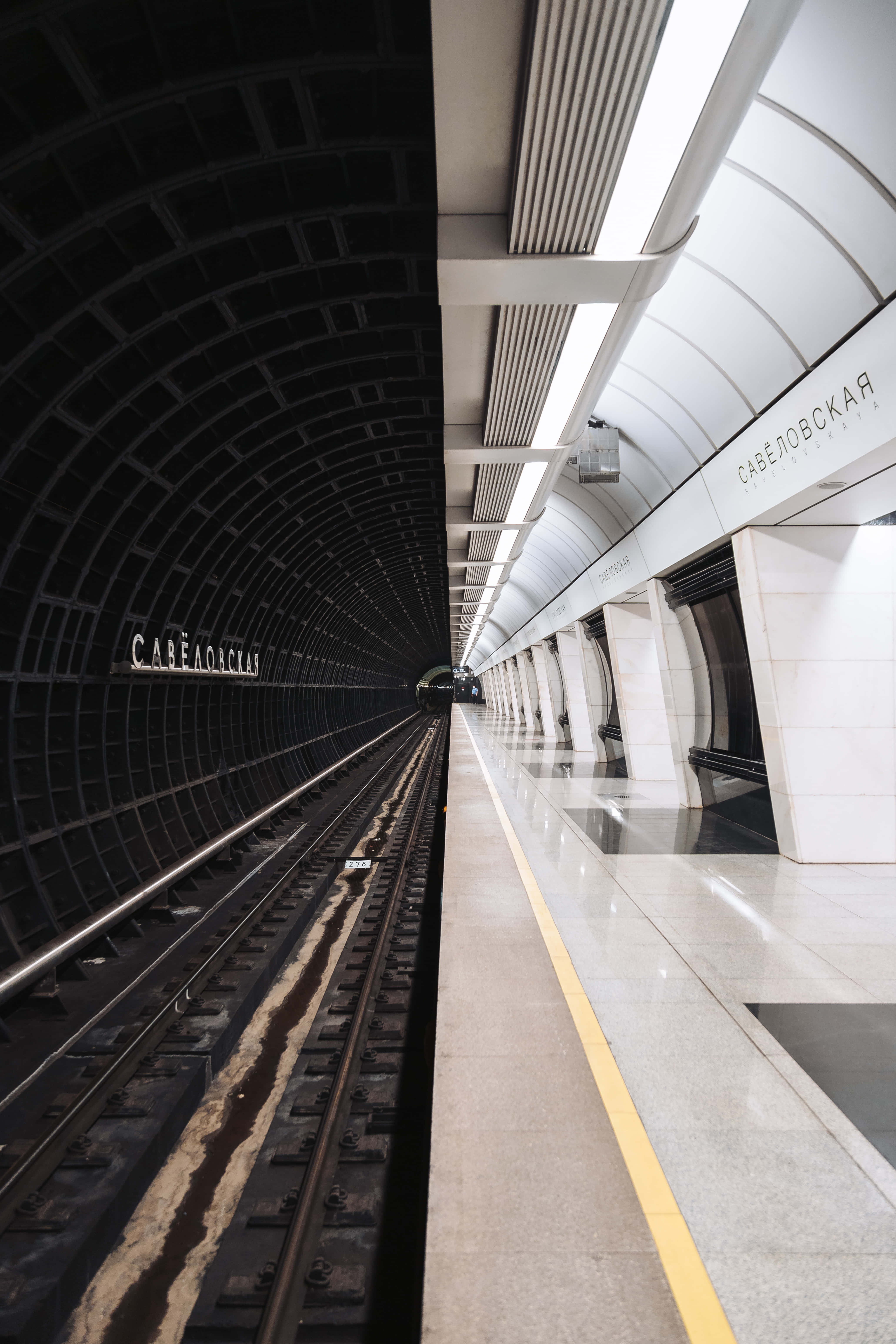Metro 桌布 壁紙 — 一個時尚現代的地鐵站，設有白色瓷磚月台和一條深色拱形隧道延伸至遠方。