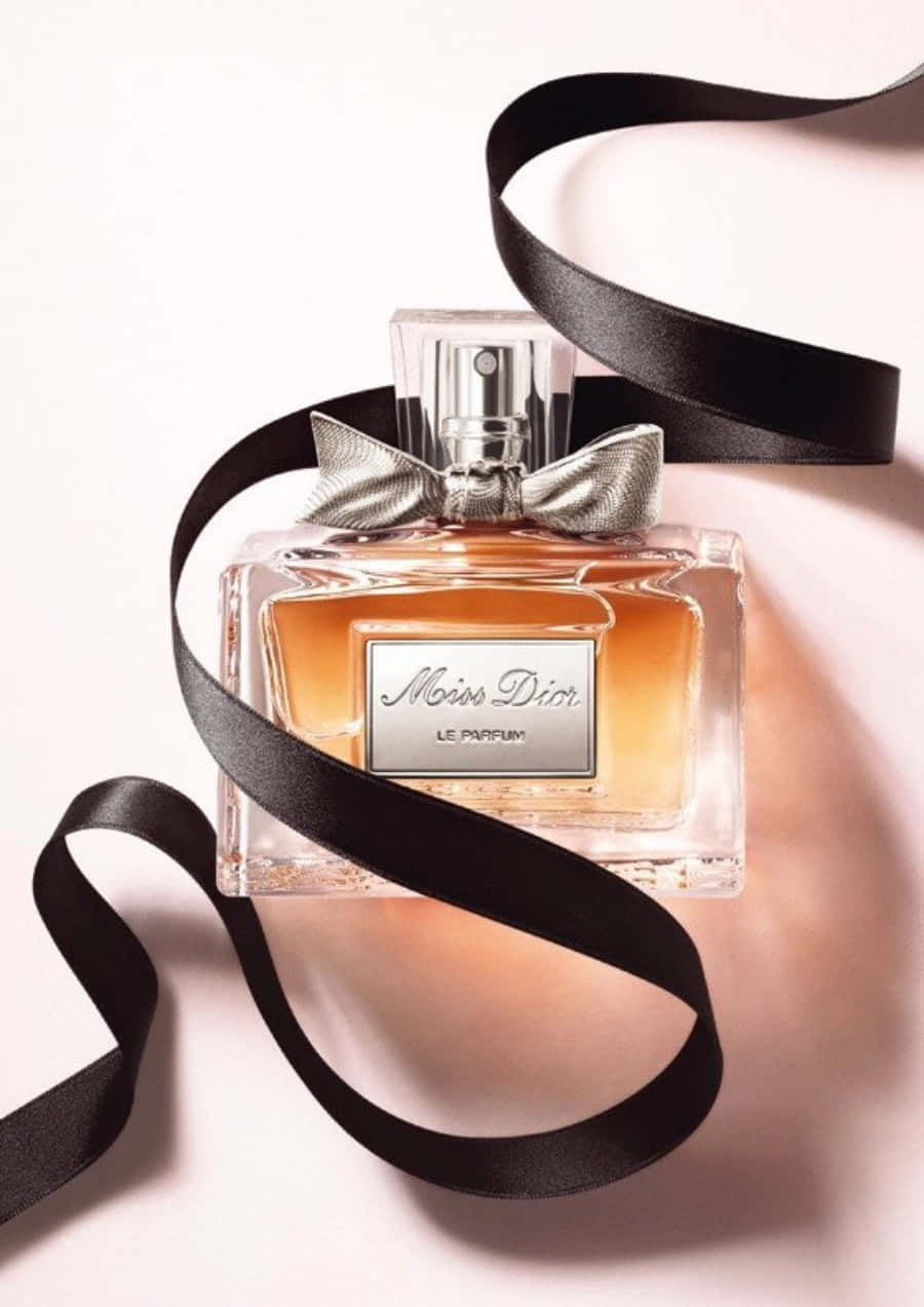 Dior 動態 桌布 壁紙 — 一個時尚的 Miss Dior 香水瓶，裝有琥珀色液體和銀色蝴蝶結，放置在柔軟的粉紅色表面上，包裹著流動的黑色絲帶。