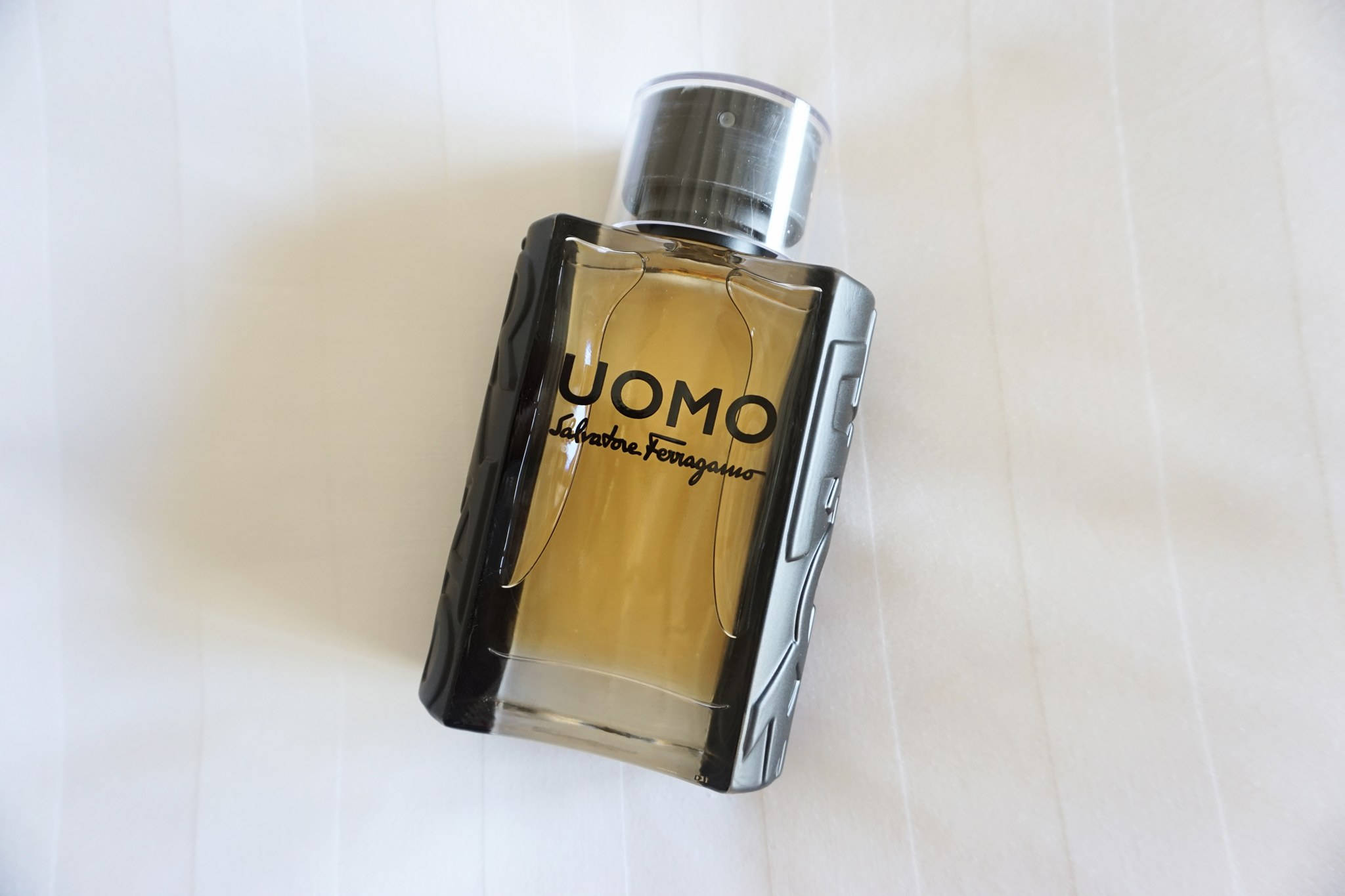 Ferragamo 桌布 壁紙 — 一個時尚的 Salvatore Ferragamo UOMO 香水瓶，內有琥珀色液體，放置在白色紋理表面上。