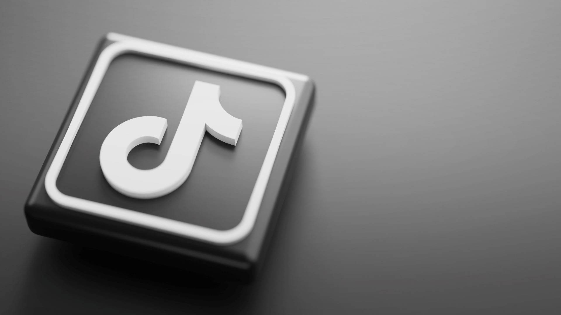 TikTok 動圖 桌布 壁紙 — 一個時尚的3D渲染TikTok標誌圖標，白色音符在黑色正方形上，放置在深灰色表面上。