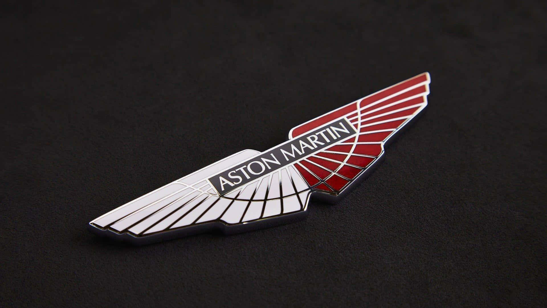 奧斯頓馬丁 桌布 壁紙 — 一個時尚的Aston Martin翼形標誌徽章，帶有紅色和銀色琺瑯，放置在霧面黑色表面上。