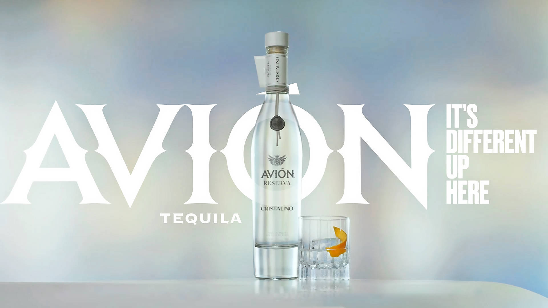 bottle 桌布 壁紙 — 一個時尚的Avion龍舌蘭酒瓶和帶有橙片的玻璃杯放在白色表面上，背景為柔和的漸變色，並帶有粗體白色字體。