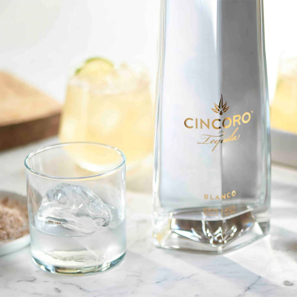 drinks 桌布 壁紙 — 一個時尚的Cincoro Blanco龍舌蘭酒瓶放在大理石檯面上，旁邊是一個加冰的古典杯。