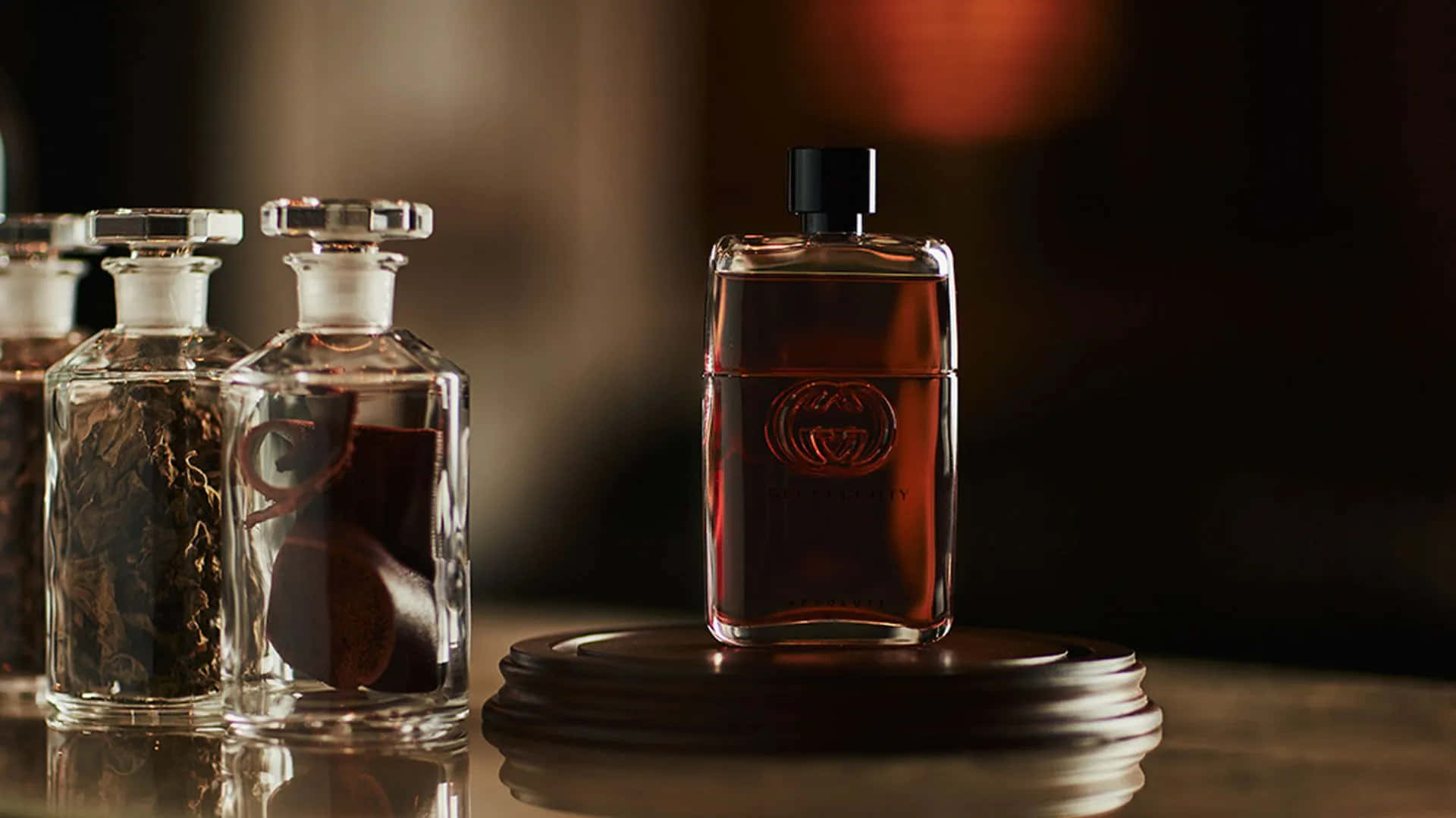 Gucci 桌布 壁紙 — 一個時尚的Gucci香水瓶，內有琥珀色液體，置於木架中央，旁邊是裝滿乾燥植物的玻璃罐，在溫暖昏暗的燈光下。