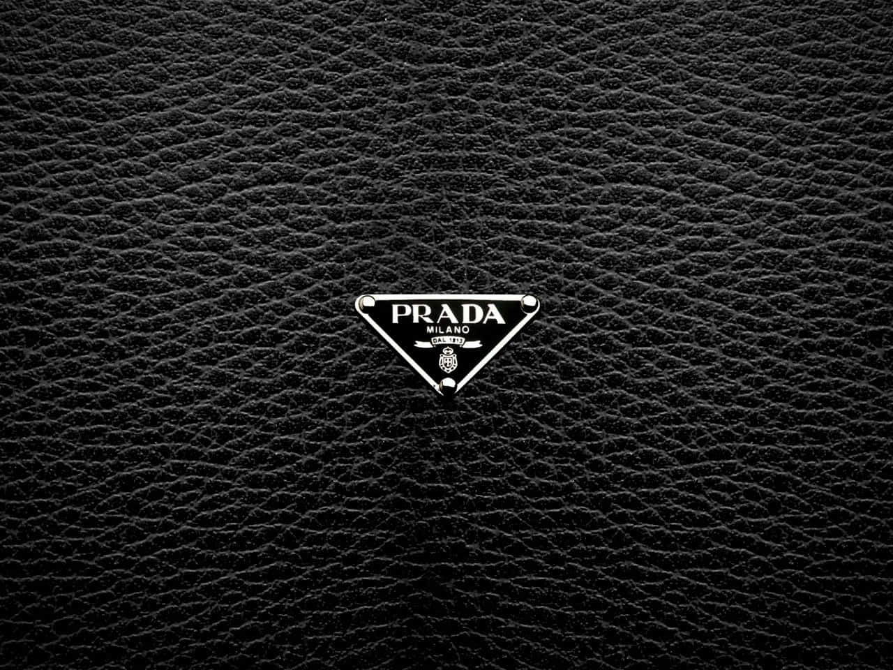 Prada 桌布 壁紙 — 一個時尚的Prada標誌徽章，居中於帶有金屬銀色飾邊的紋理黑色皮革上。