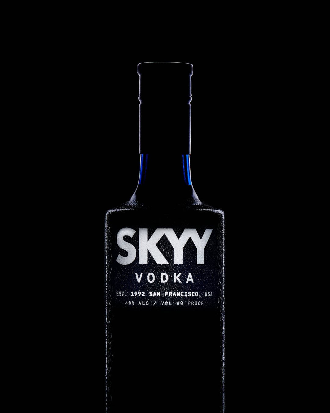 Drink 桌布 壁紙 — 一個時尚的Skyy Vodka酒瓶居中放置在純黑色背景上，其標籤閃耀著清晰的白字和微妙的藍色點綴。