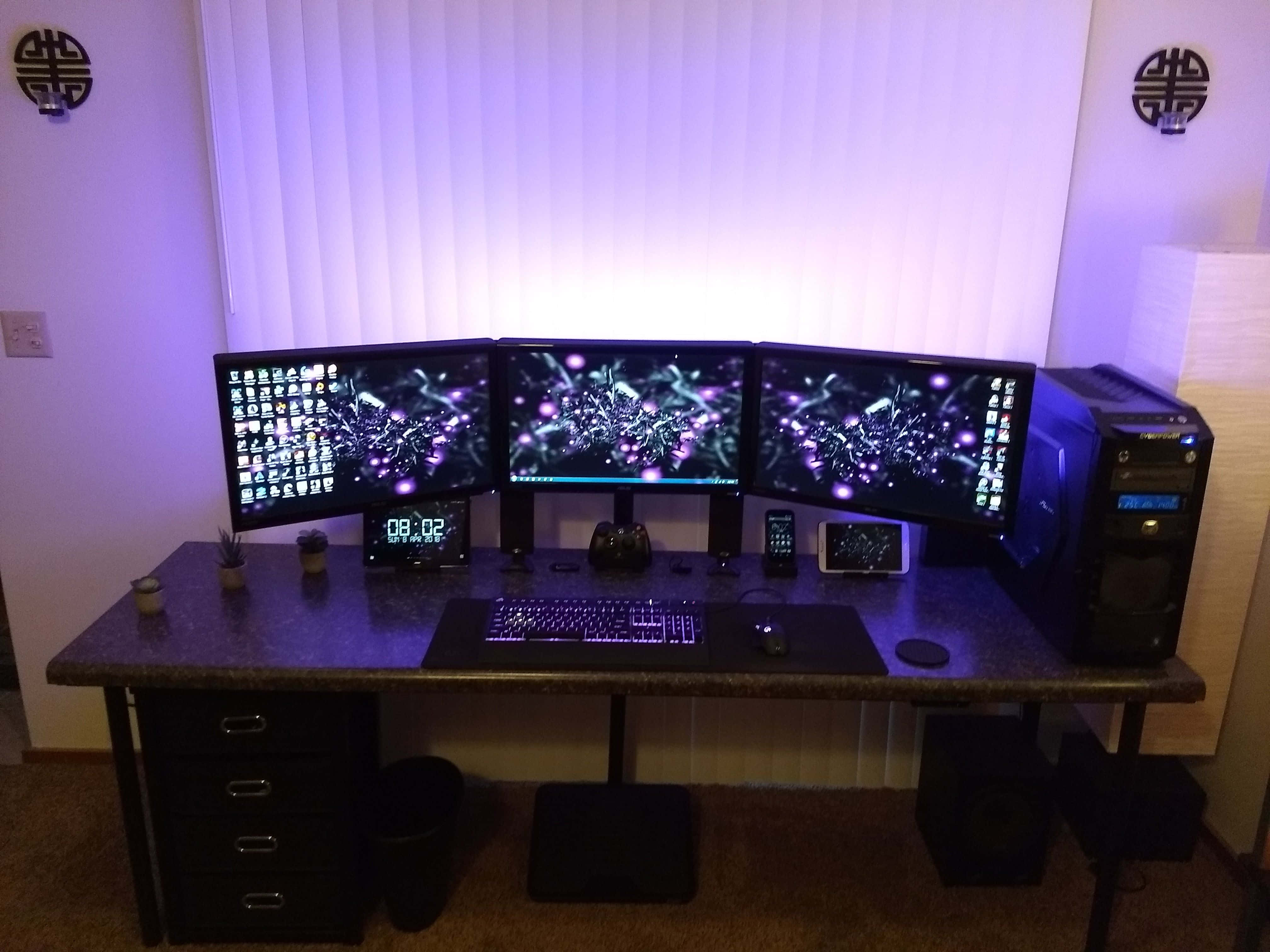 Gaming Pc Setup 桌布 壁紙 — 一個時尚的三顯示器遊戲設置，沐浴在紫色LED光芒中，在深色桌子上配有鍵盤、滑鼠和PC主機。