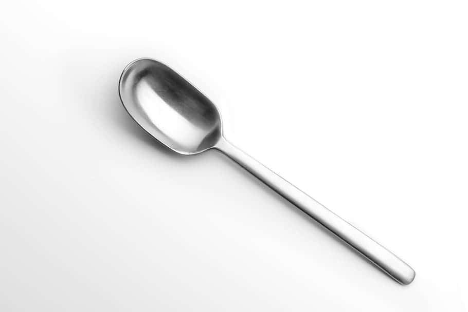 kitchen 桌布 壁紙 — 一個時尚的不鏽鋼湯匙斜放在純白表面上，其拋光曲線捕捉柔和光線。