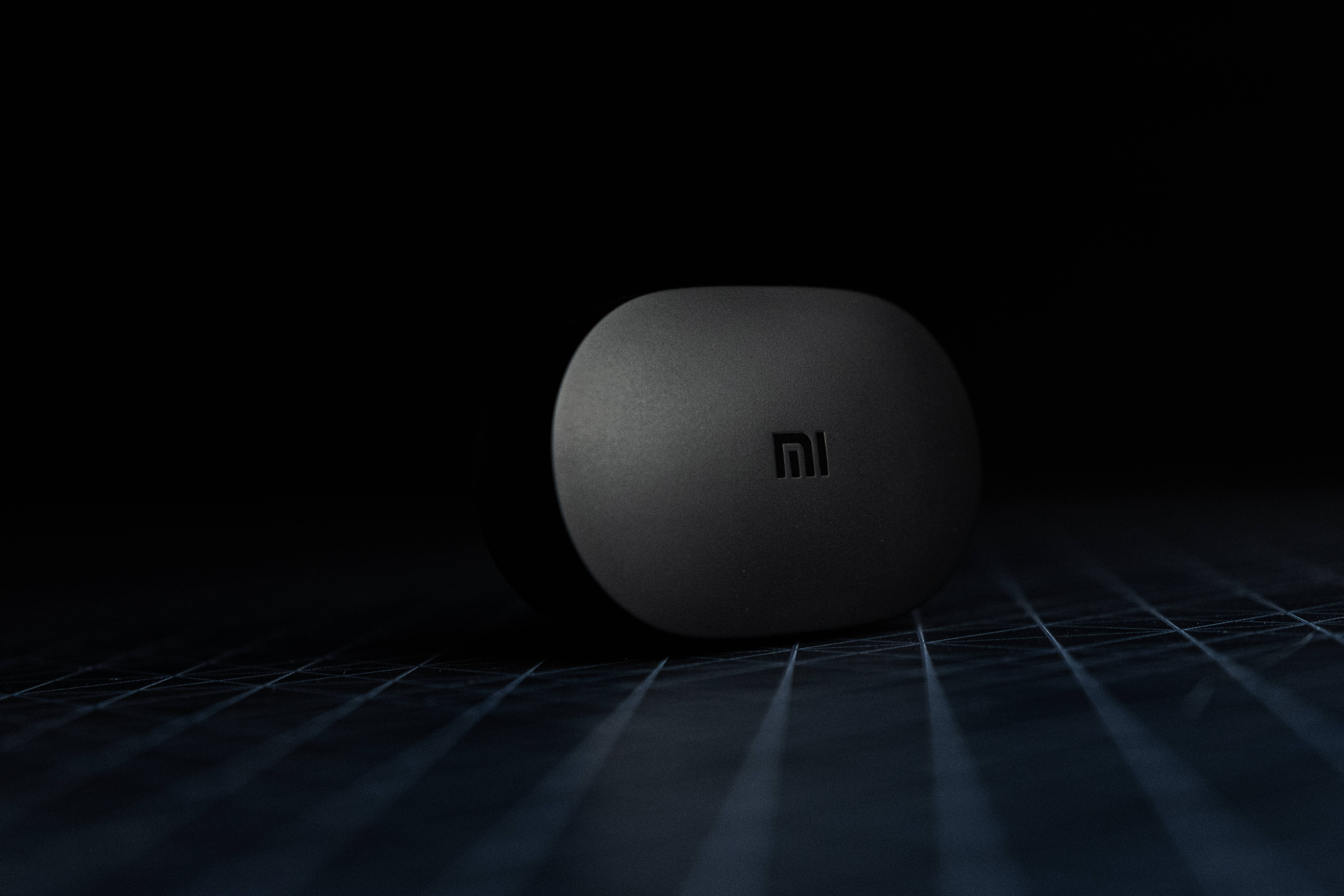 Xiaomi 桌布 壁紙 — 一個時尚的啞光黑色Xiaomi耳機盒放置在深色網格表面上，在戲劇性的聚光燈下。