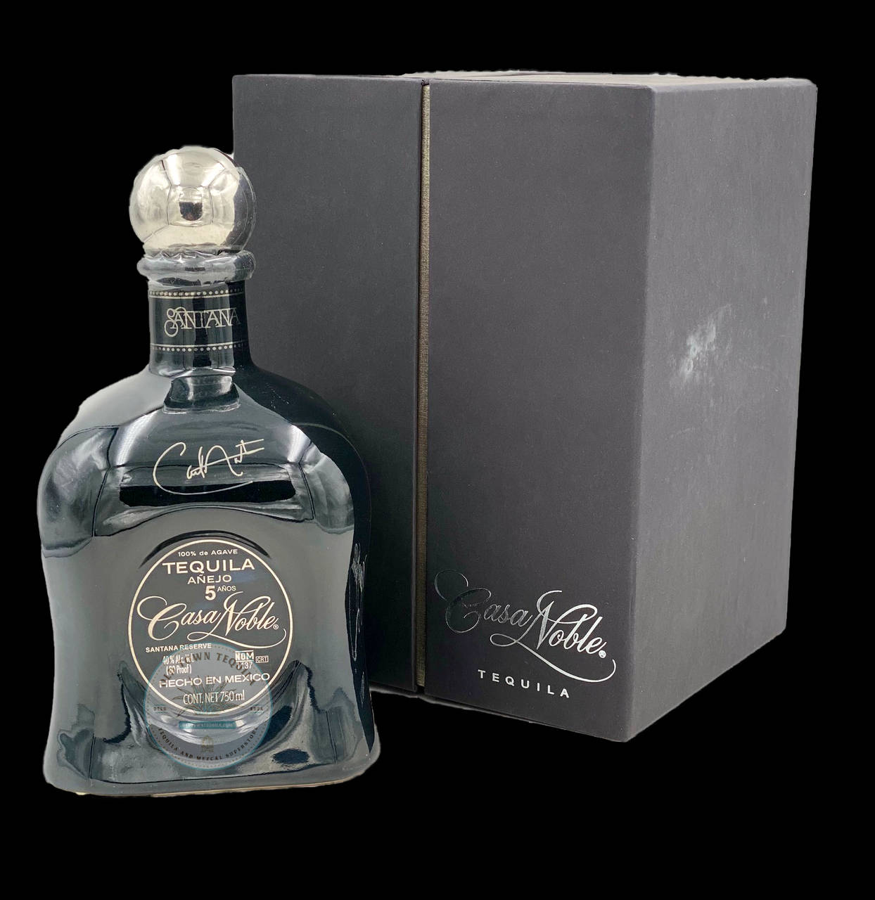 Tequila 桌布 壁紙 — 一個時尚的深藍色Casa Noble龍舌蘭酒瓶配銀色瓶蓋，旁邊放著它的啞光黑色盒子，背景是純黑色。