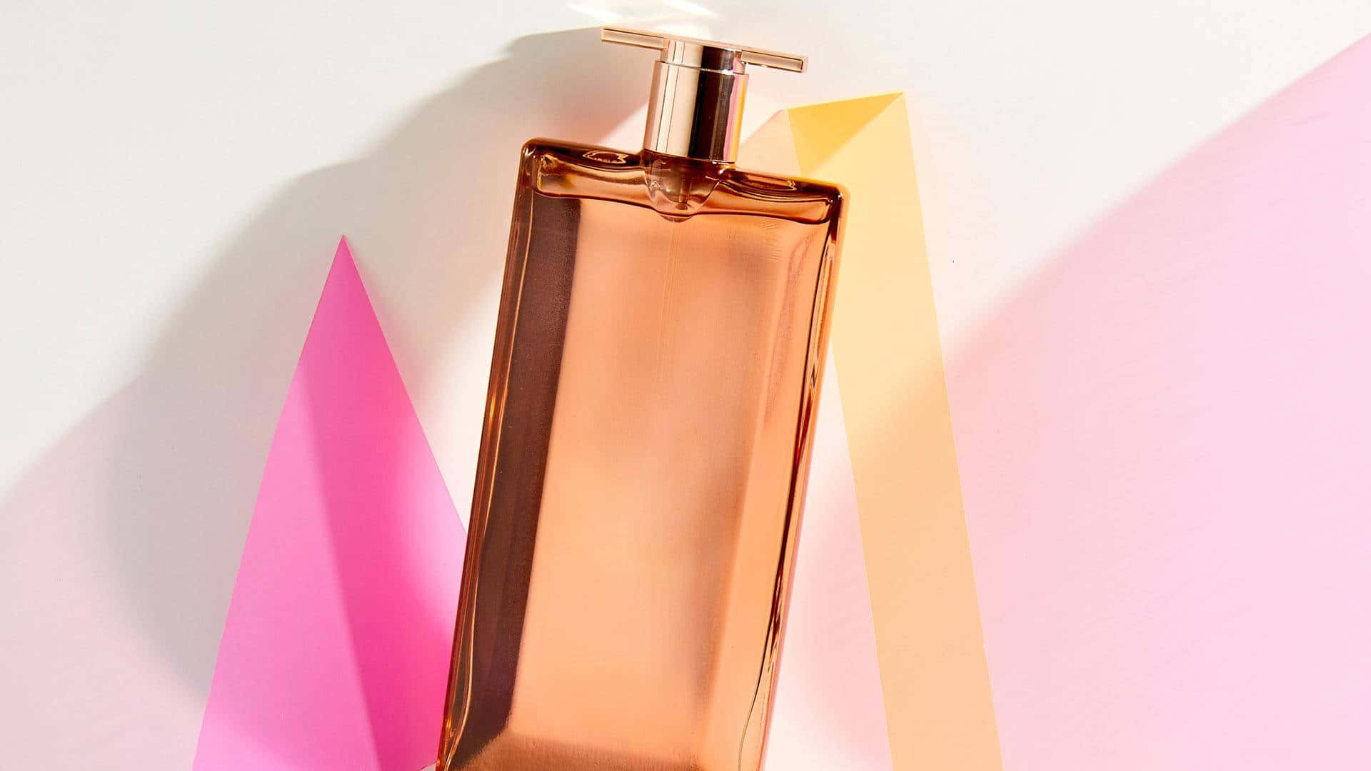 Spring Perfume 桌布 壁紙 — 一個時尚的玫瑰金香水瓶在粉彩粉紅和黃色幾何背景上投下柔和陰影。