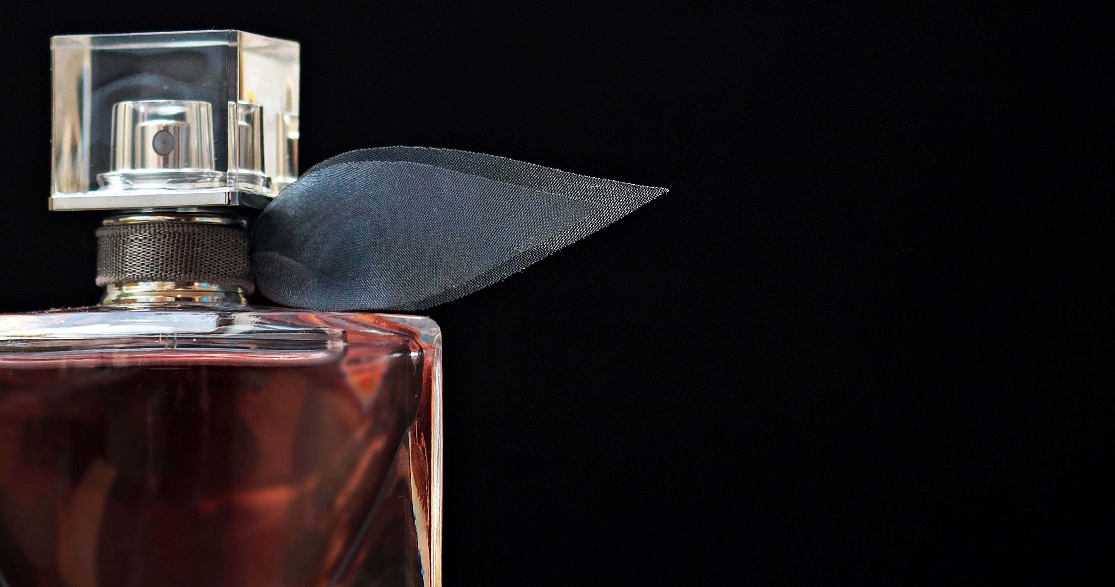Fragrance 桌布 壁紙 — 一個時尚的玻璃香水瓶，帶有深色絲帶，襯托在純黑背景上。