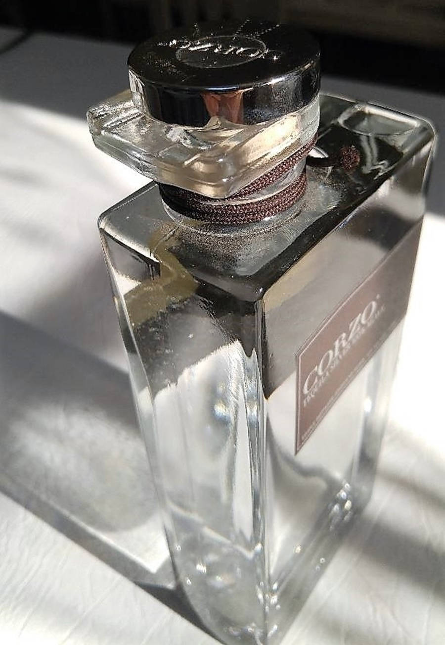 bottle 桌布 壁紙 — 一個時尚的玻璃香水瓶，帶有黑色瓶蓋和棕色標籤，放在白色紋理表面上，在明亮的陽光下。