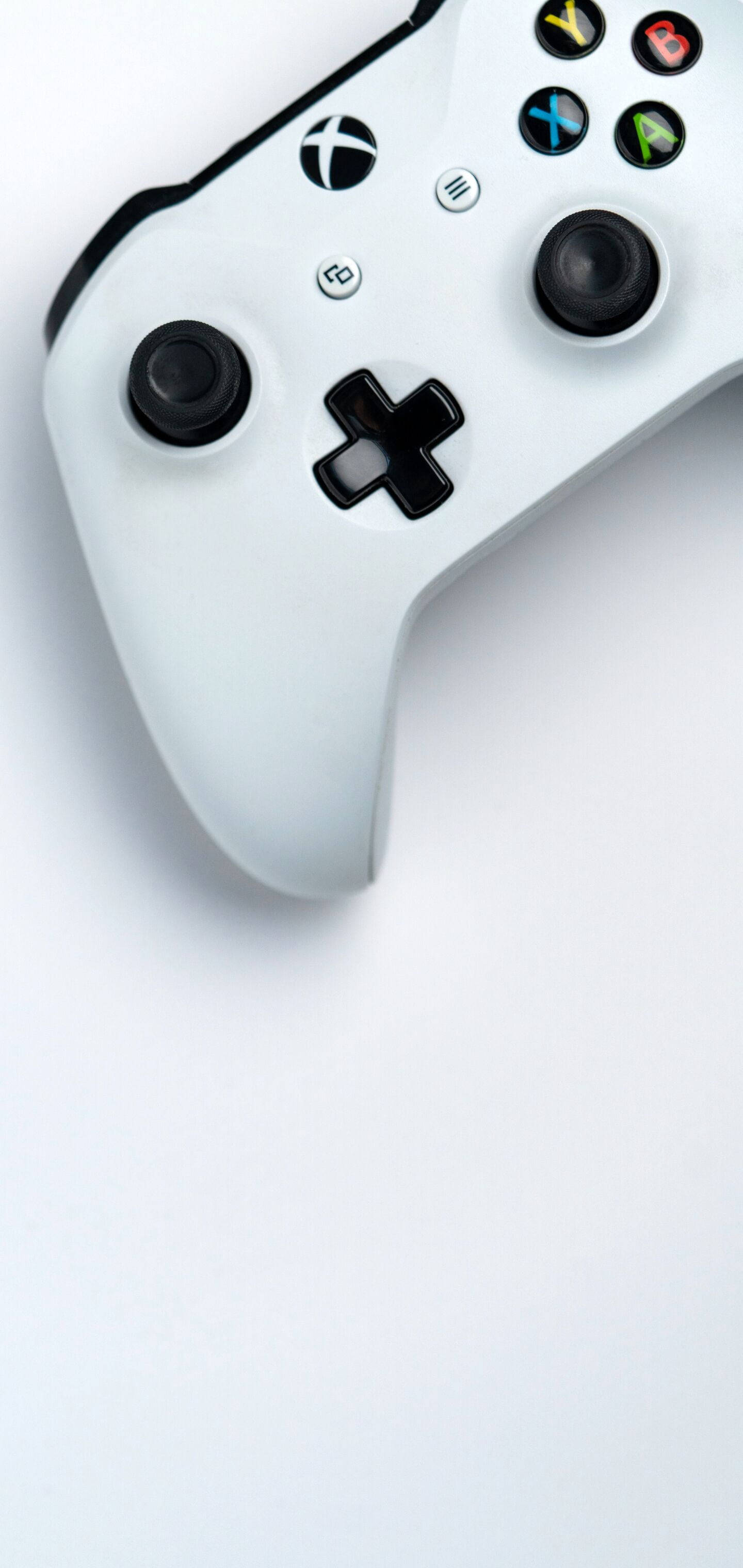 Xbox 桌布 壁紙 — 一個時尚的白色Xbox手把斜放在簡約的白色表面上，突顯其符合人體工學的設計和標誌性的按鈕佈局。