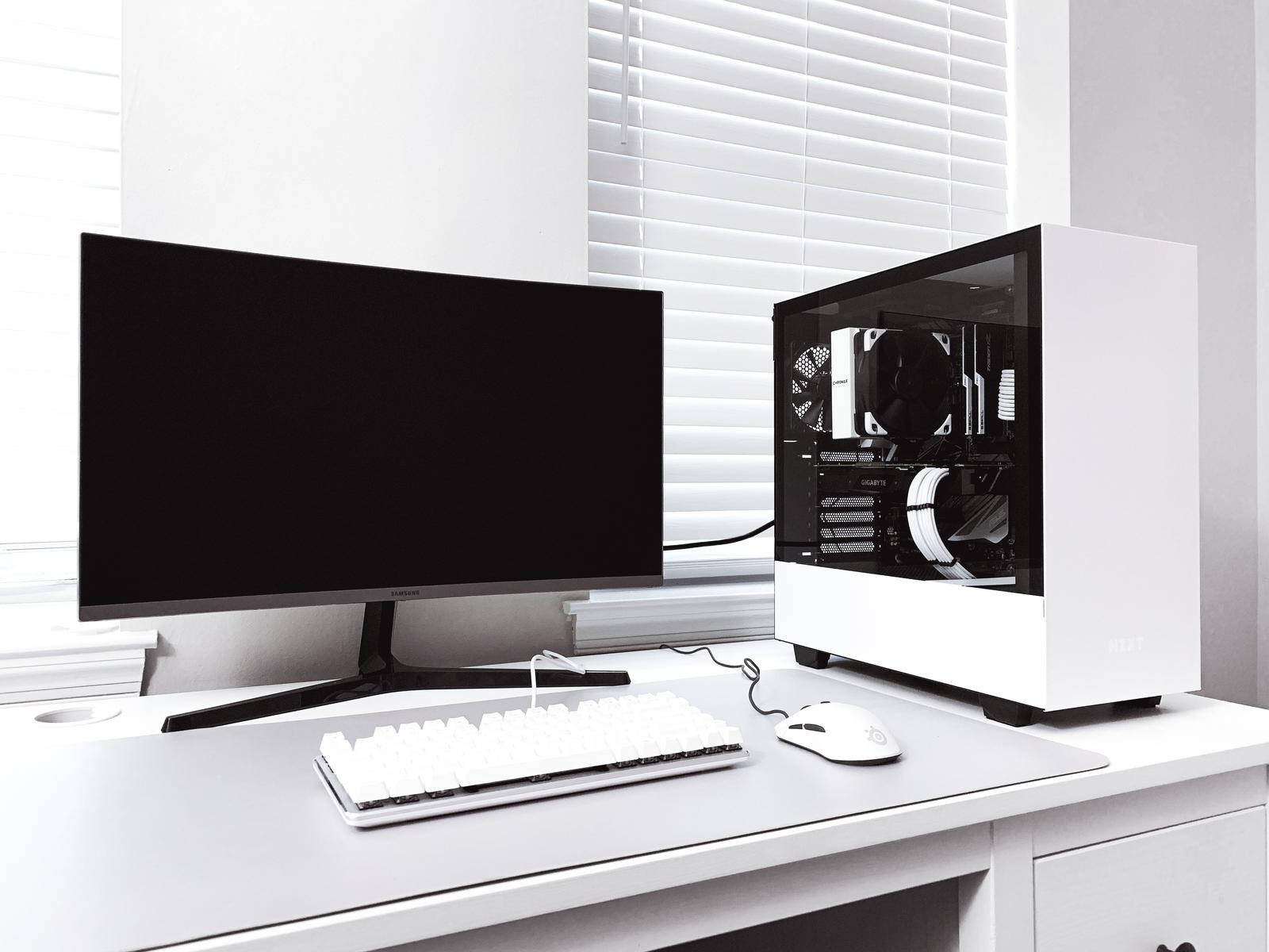 White Pc 桌布 壁紙 — 一個時尚的白色遊戲設置，配備曲面顯示器、鍵盤、滑鼠和透明機殼，放置在百葉窗附近的簡約桌子上。