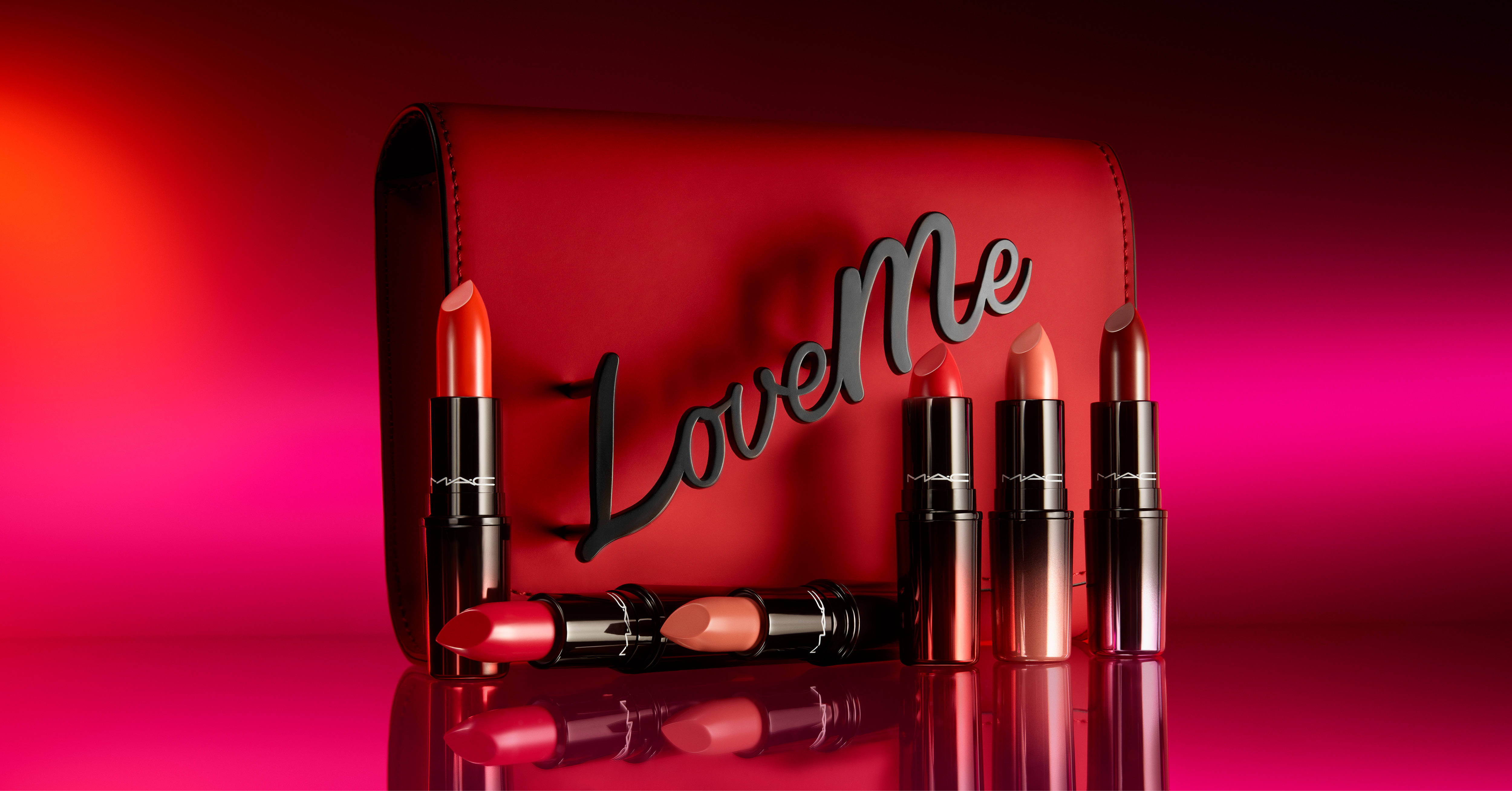Cosmetics 桌布 壁紙 — 一個時尚的紅色MAC唇膏盒，上面有黑色的「LoveMe」字樣，周圍是鮮豔的紅色和粉紅色唇膏，放在漸變反射表面上。