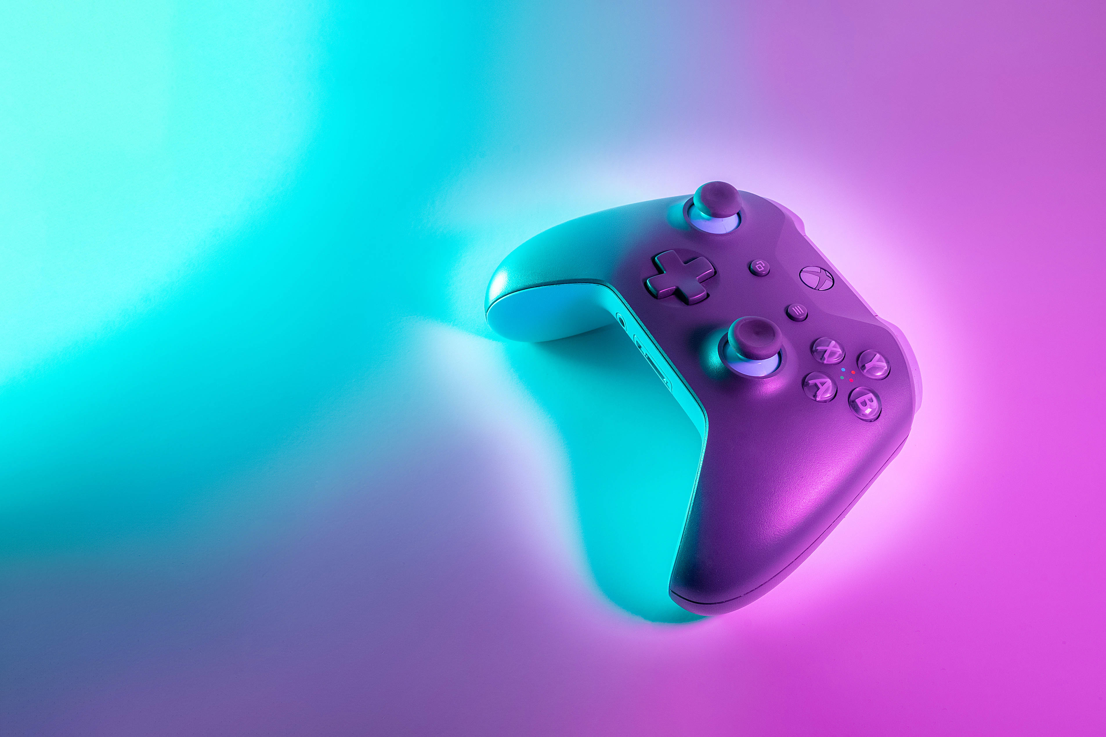 Xbox 桌布 壁紙 — 一個時尚的紫色遊戲控制器，沐浴在發光的青色和洋紅色光線中，背景為漸變色。