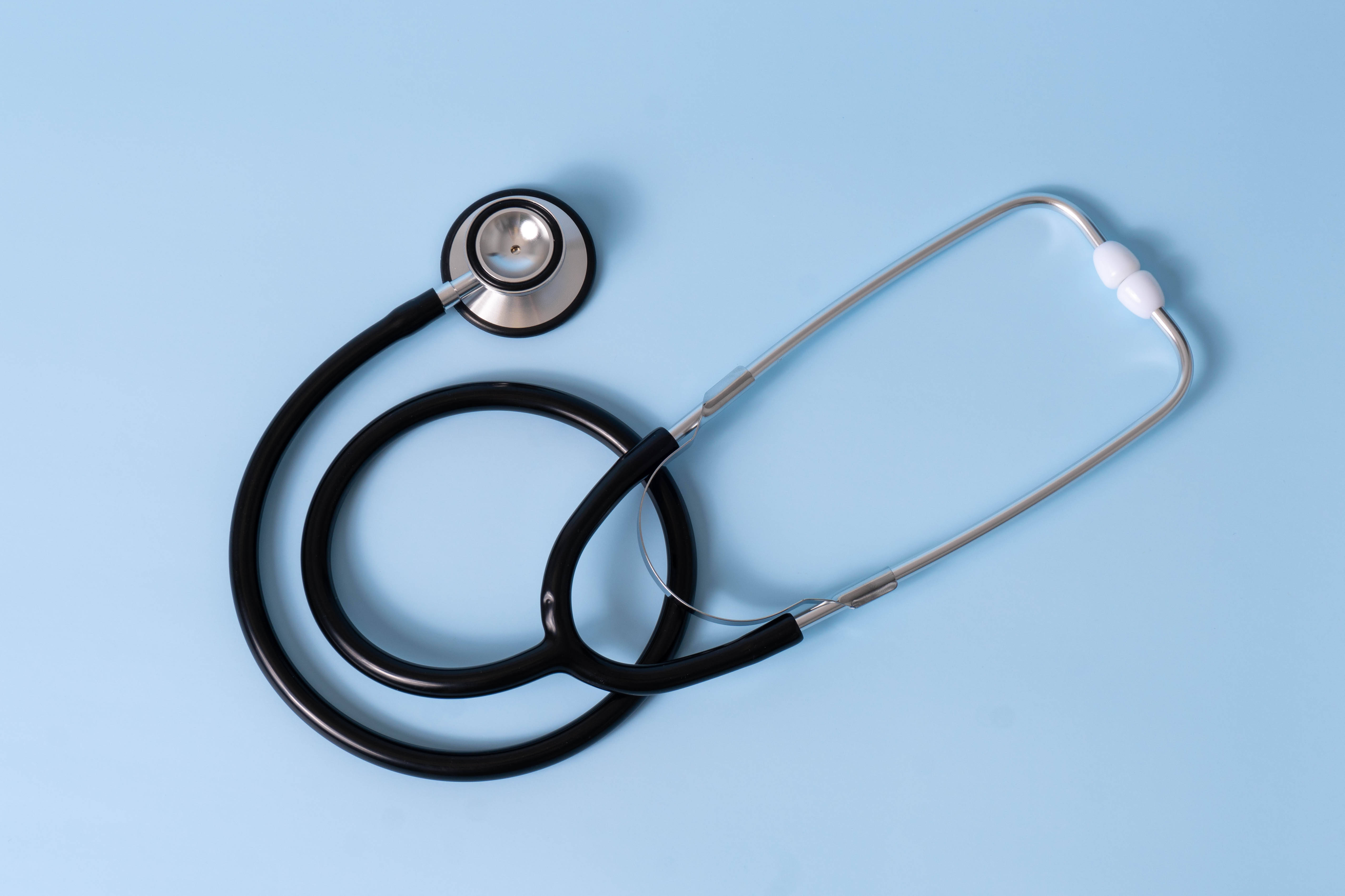 Stethoscope 桌布 壁紙 — 一個時尚的聽診器，帶有黑色軟管和銀色胸件，盤繞在柔和的藍色背景上。