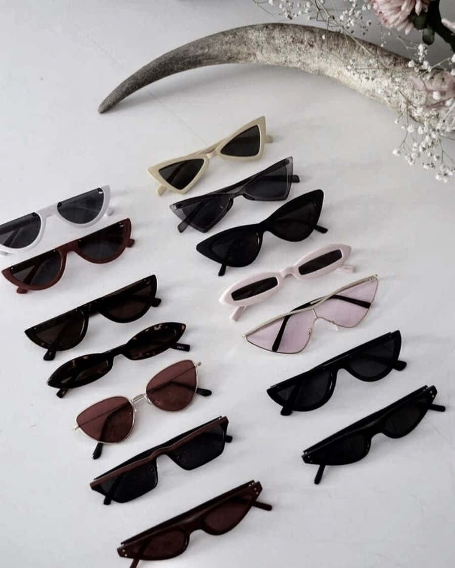 Sunglasses 桌布 壁紙 — 一個時尚的貓眼太陽眼鏡系列，各種顏色排列在白色表面上，配有裝飾角及乾花。