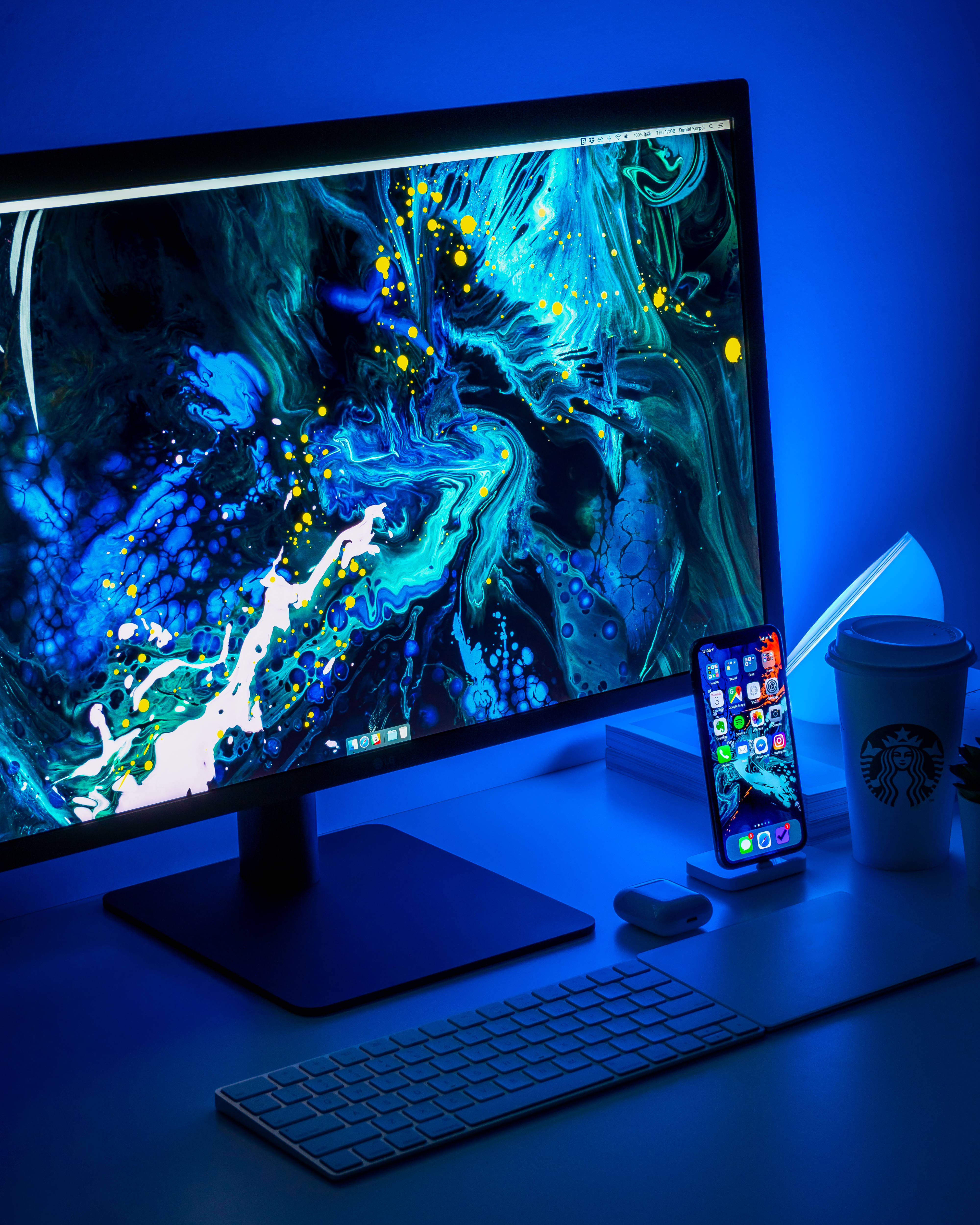 broken monitor 桌布 壁紙 — 一個時尚的辦公桌設置沐浴在藍光中，顯示器展示了一個充滿活力的抽象壁紙，帶有旋轉的藍綠色和黃色圖案。