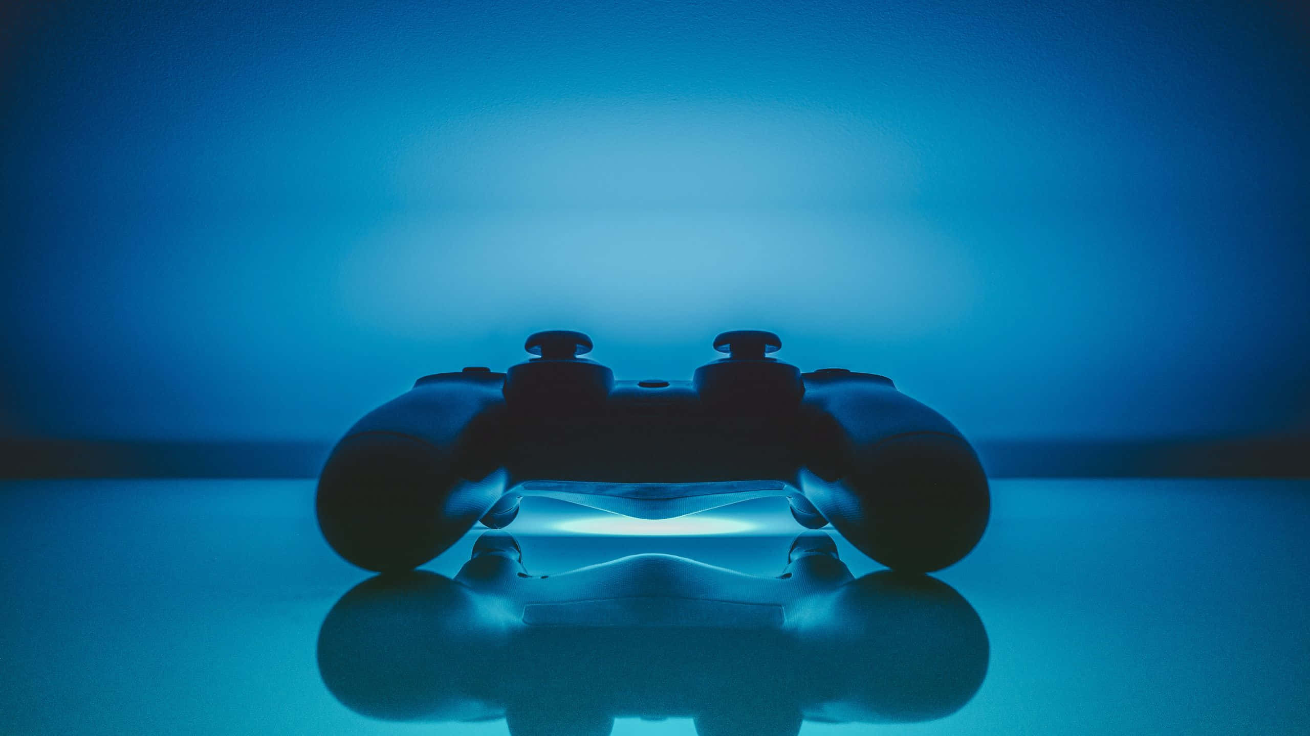 Gaming Banner 桌布 壁紙 — 一個時尚的遊戲控制器在反光表面上發出藍光，背景為漸變藍色。