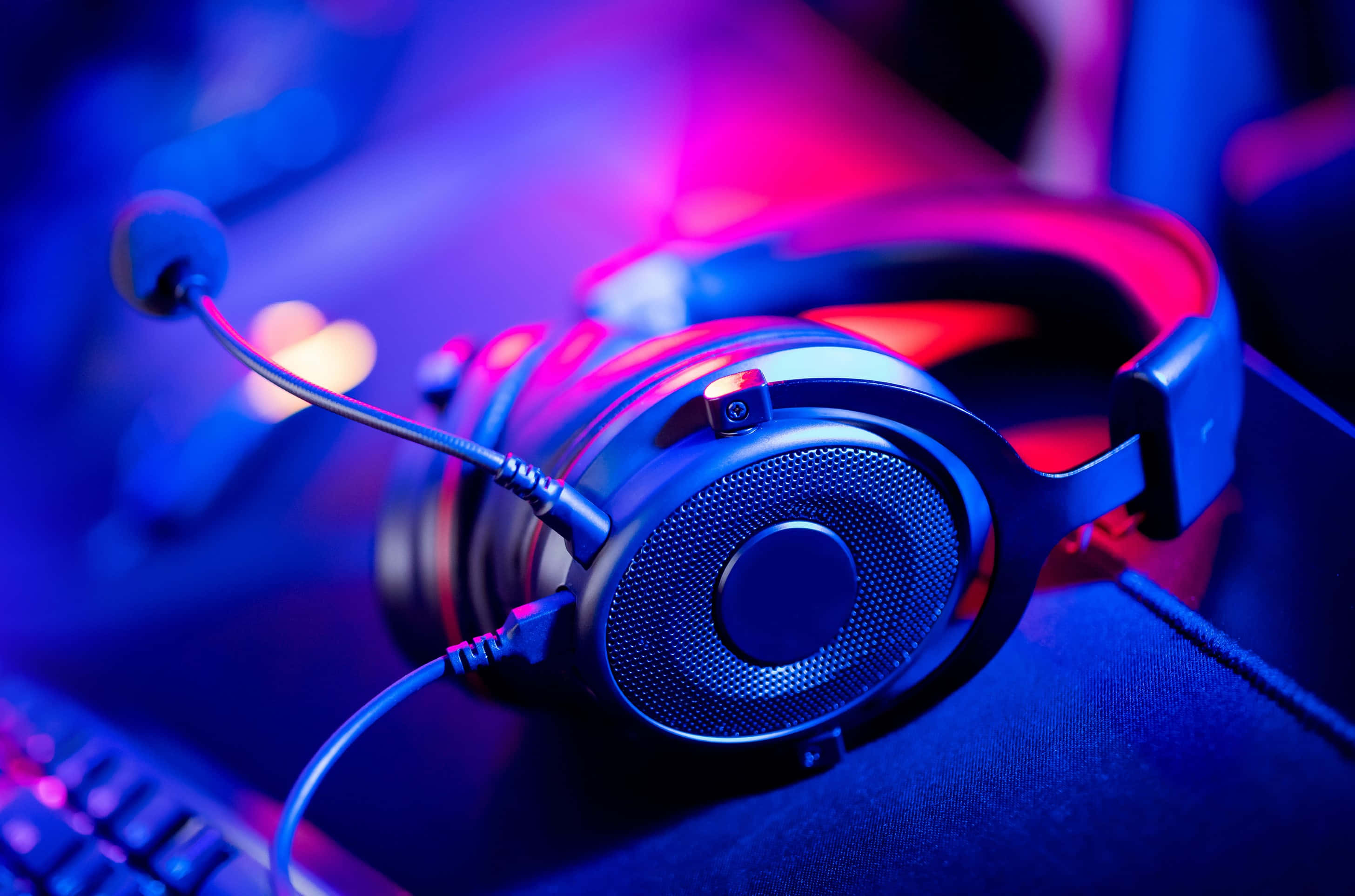 Gaming Headsets 桌布 壁紙 — 一個時尚的遊戲耳機連麥克風放在鍵盤上，在鮮豔的藍色和粉紅色霓虹燈光下。