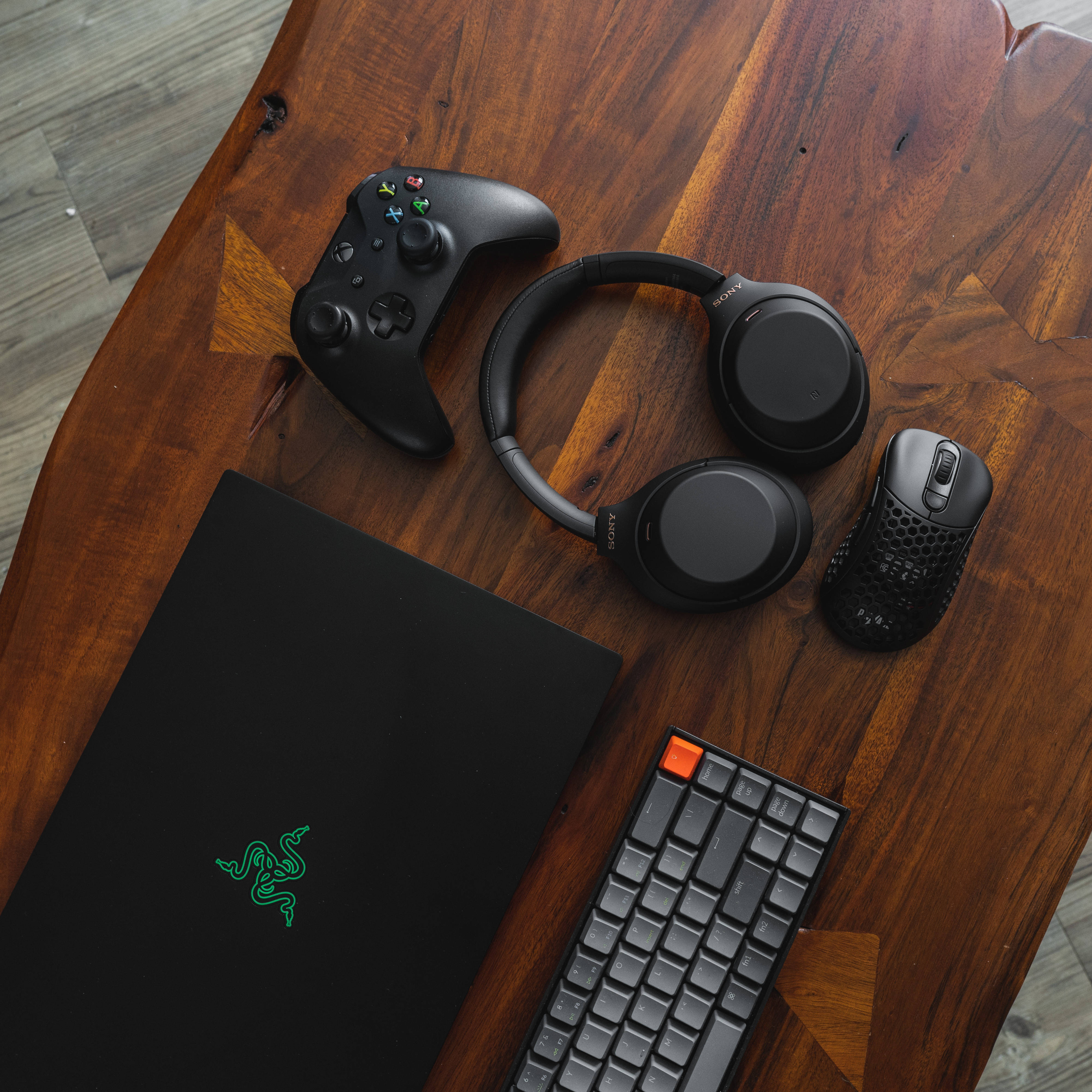 雷蛇 桌布 壁紙 — 一個時尚的遊戲設置，配備 Razer 筆記型電腦、鍵盤、控制器、耳機和滑鼠，排列在豐富的木桌上。