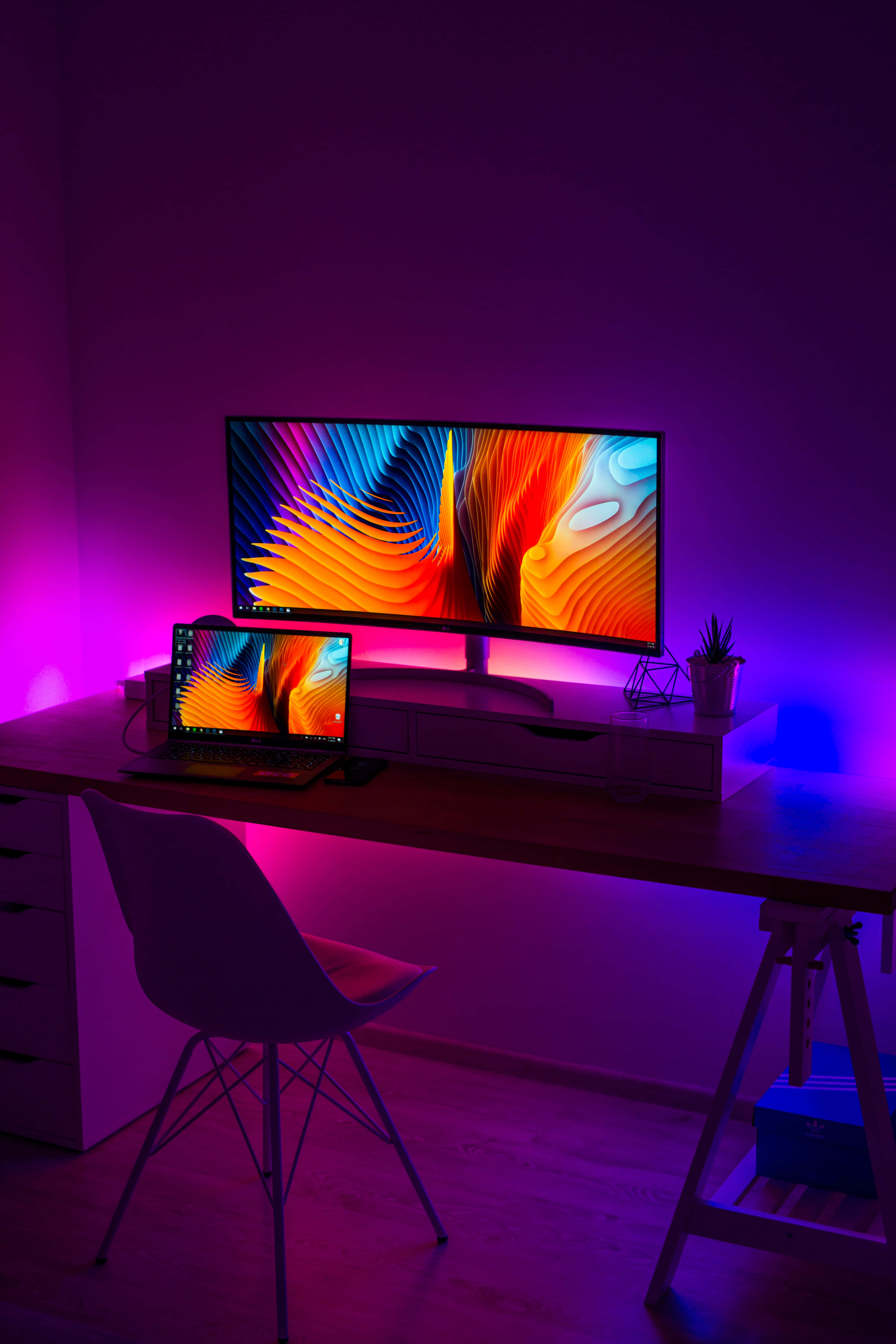 Monitor 桌布 壁紙 — 一個時尚的遊戲設置，配備曲面顯示器和筆記型電腦，在紫色環境燈光下散發著充滿活力的抽象桌布光芒。