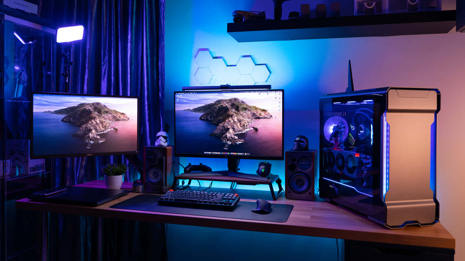 Gaming Pc Setup 桌布 壁紙 — 一個時尚的遊戲設置，配備雙顯示器，顯示日落時分的岩石島嶼，由鮮豔的藍色和紫色LED燈照亮。
