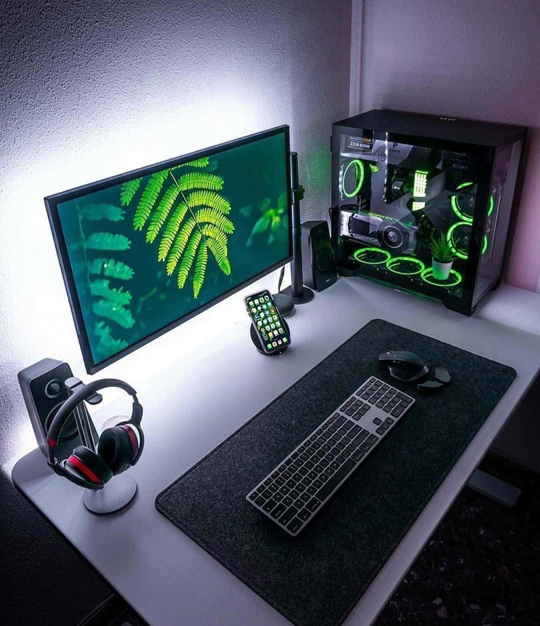 Gaming Accessories 桌布 壁紙 — 一個時尚的遊戲設置，配有發光的綠色蕨類植物壁紙、RGB 燈效 PC 機箱和現代周邊設備，在柔和環境光下。