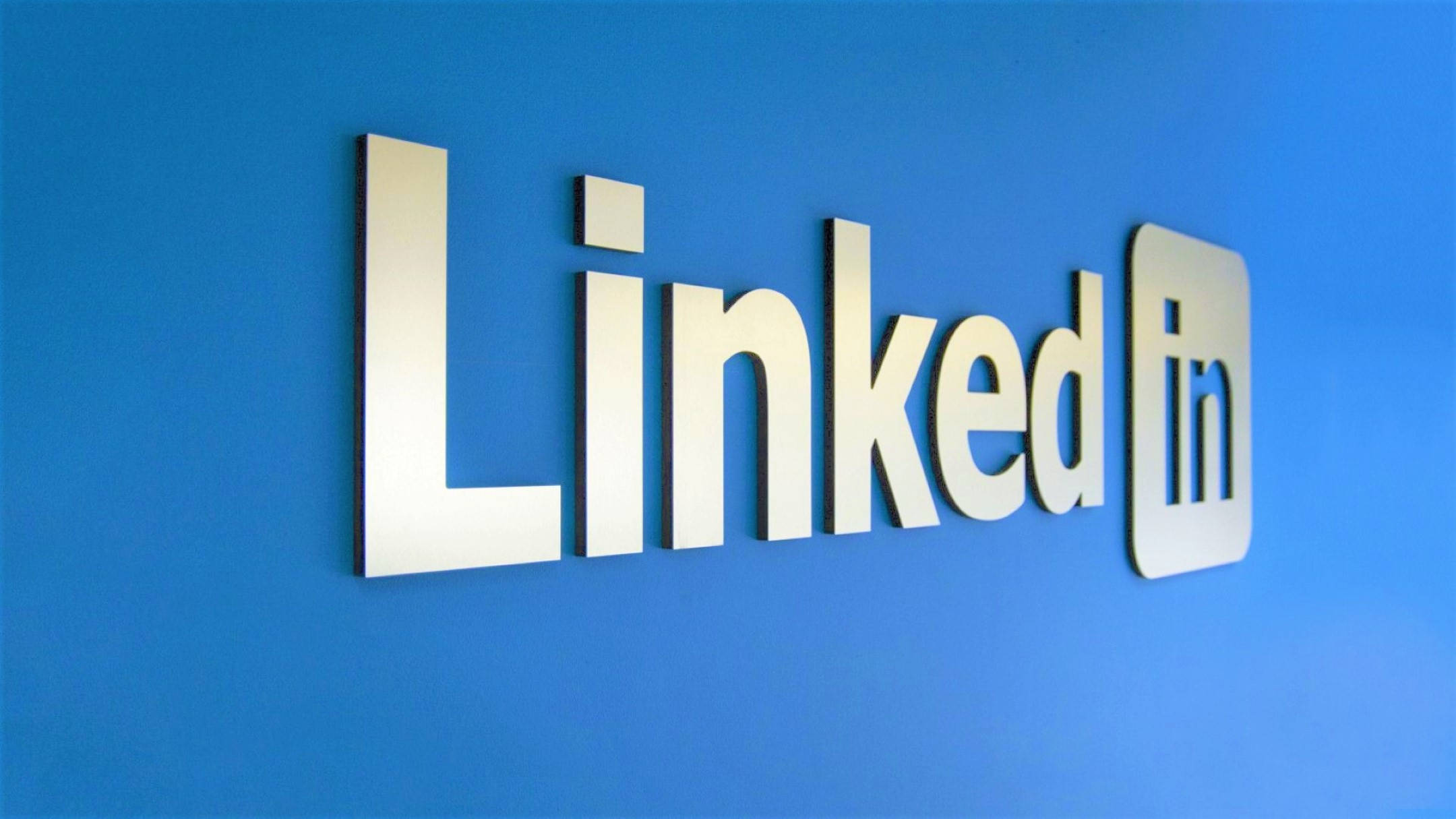 Linkedin 桌布 壁紙 — 一個時尚的金屬LinkedIn標誌安裝在現代辦公室環境中充滿活力的藍色牆壁上。