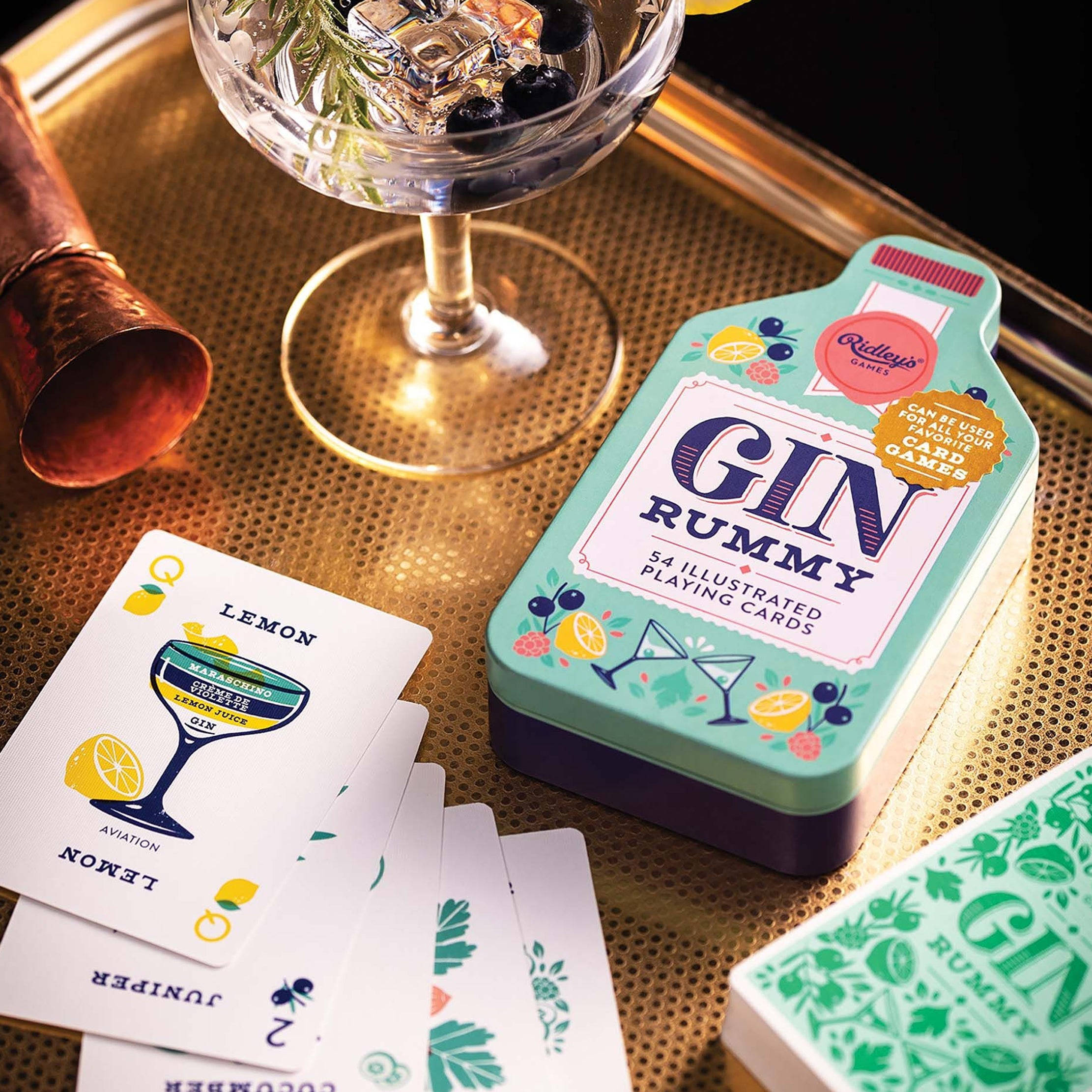 Playing Cards 桌布 壁紙 — 一個時尚的金拉米紙牌遊戲套裝，配有一個雞尾酒杯和銅製搖酒器，放在一個有紋理的金色托盤上。