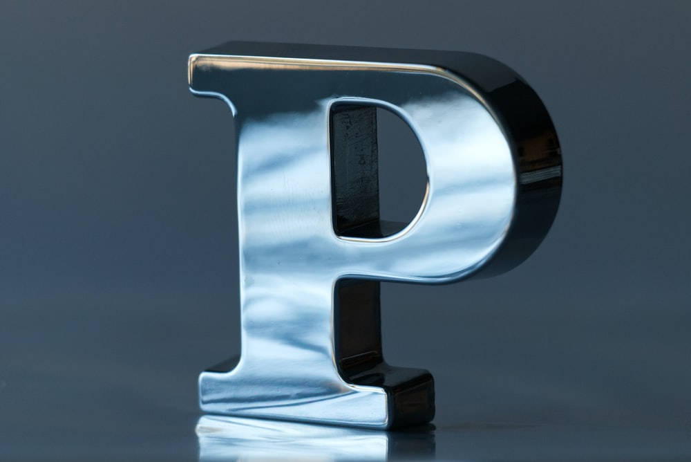 字母P 桌布 壁紙 — 一個時尚的鉻字母P高高矗立在反光表面上，背景是柔和的灰色。