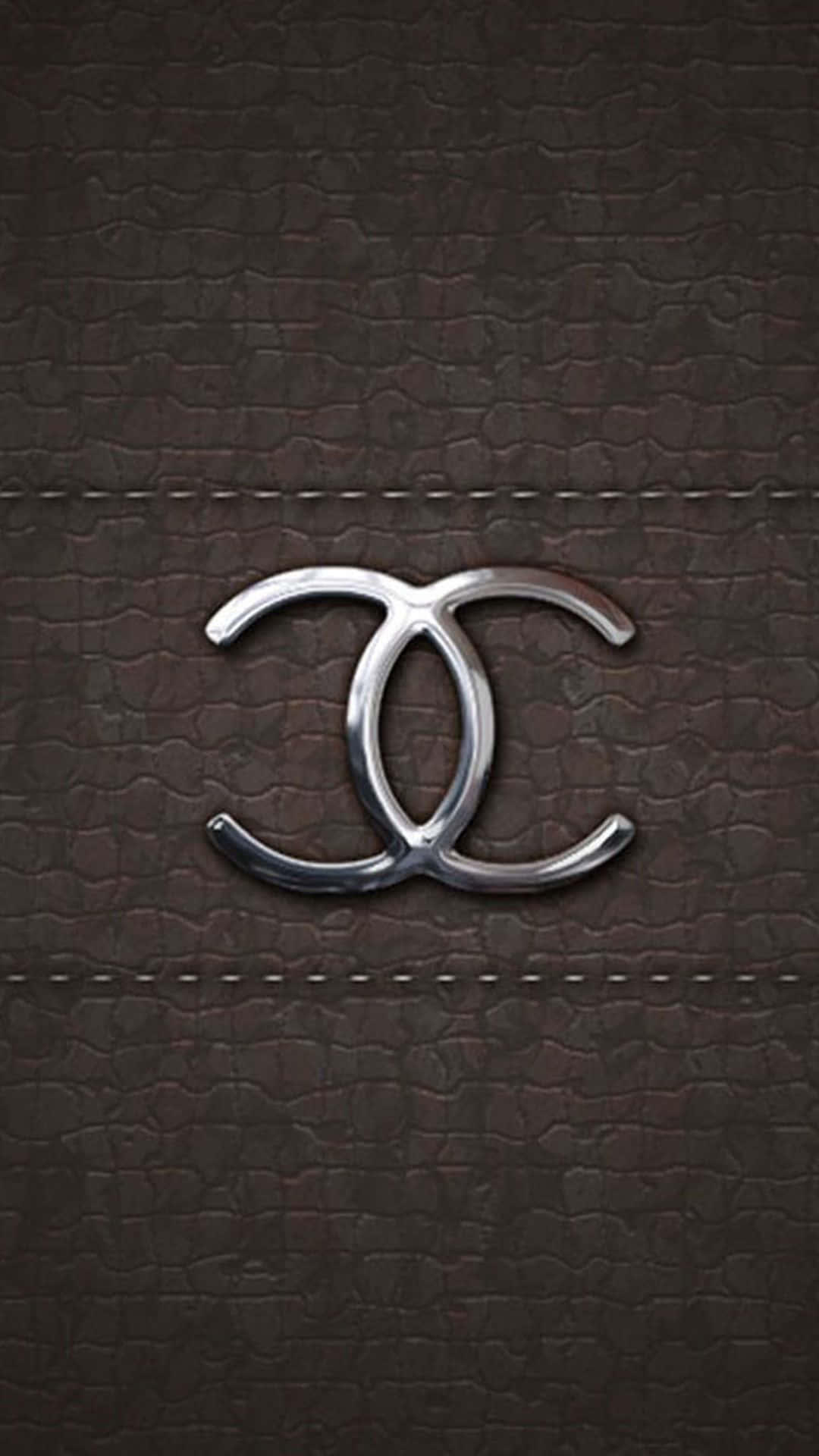香奈兒標誌 桌布 壁紙 — 一個時尚的銀色 Chanel 標誌居中放置在帶有精確縫線的濃郁棕色紋理皮革上。