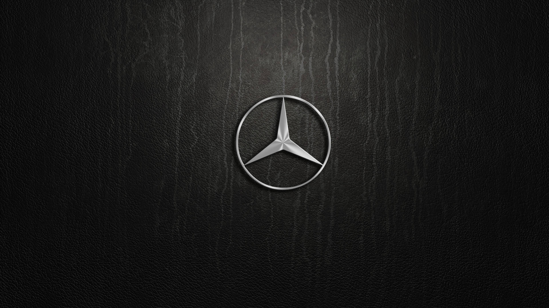 跑車 桌布 壁紙 — 一個時尚的銀色 Mercedes-Benz 標誌，置於帶有細微垂直紋理的黑色皮革表面上。
