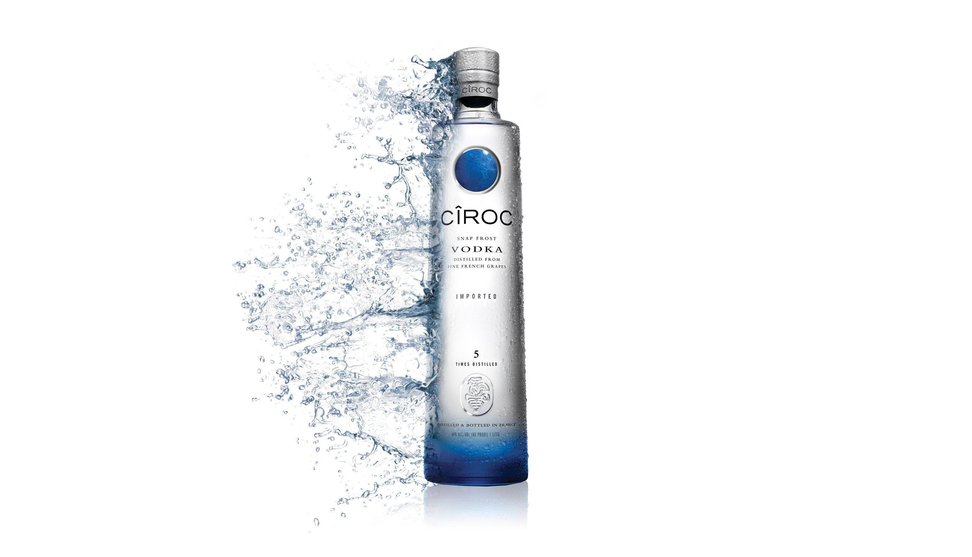 Drink 桌布 壁紙 — 一個時尚的銀色Ciroc伏特加酒瓶帶有藍色點綴，立於白色背景前，動態的水花在其底部周圍戲劇性地飛濺。