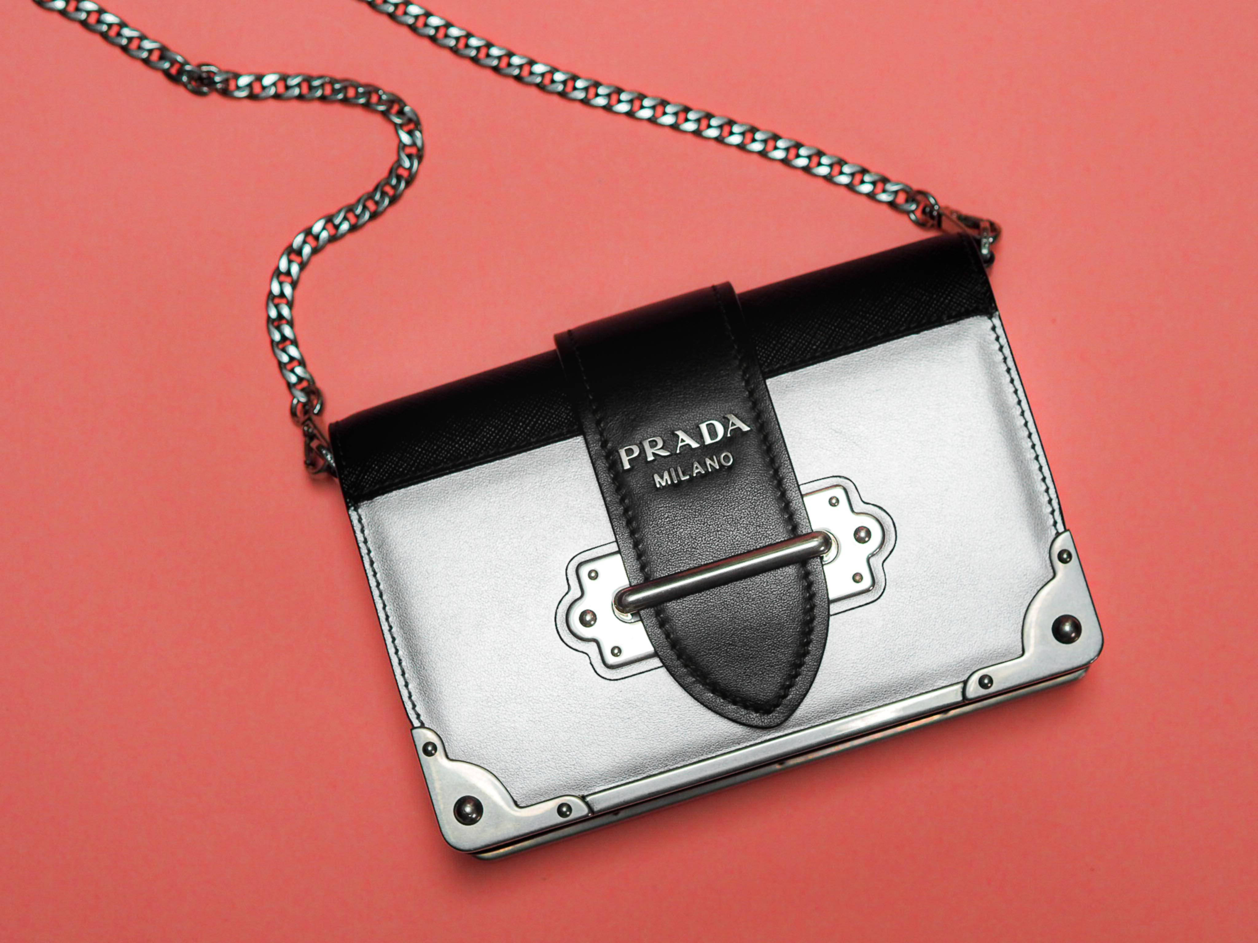 Prada 桌布 壁紙 — 一個時尚的銀色Prada手提包，帶有黑色皮革飾邊和鏈條肩帶，放在珊瑚粉紅色的背景上。
