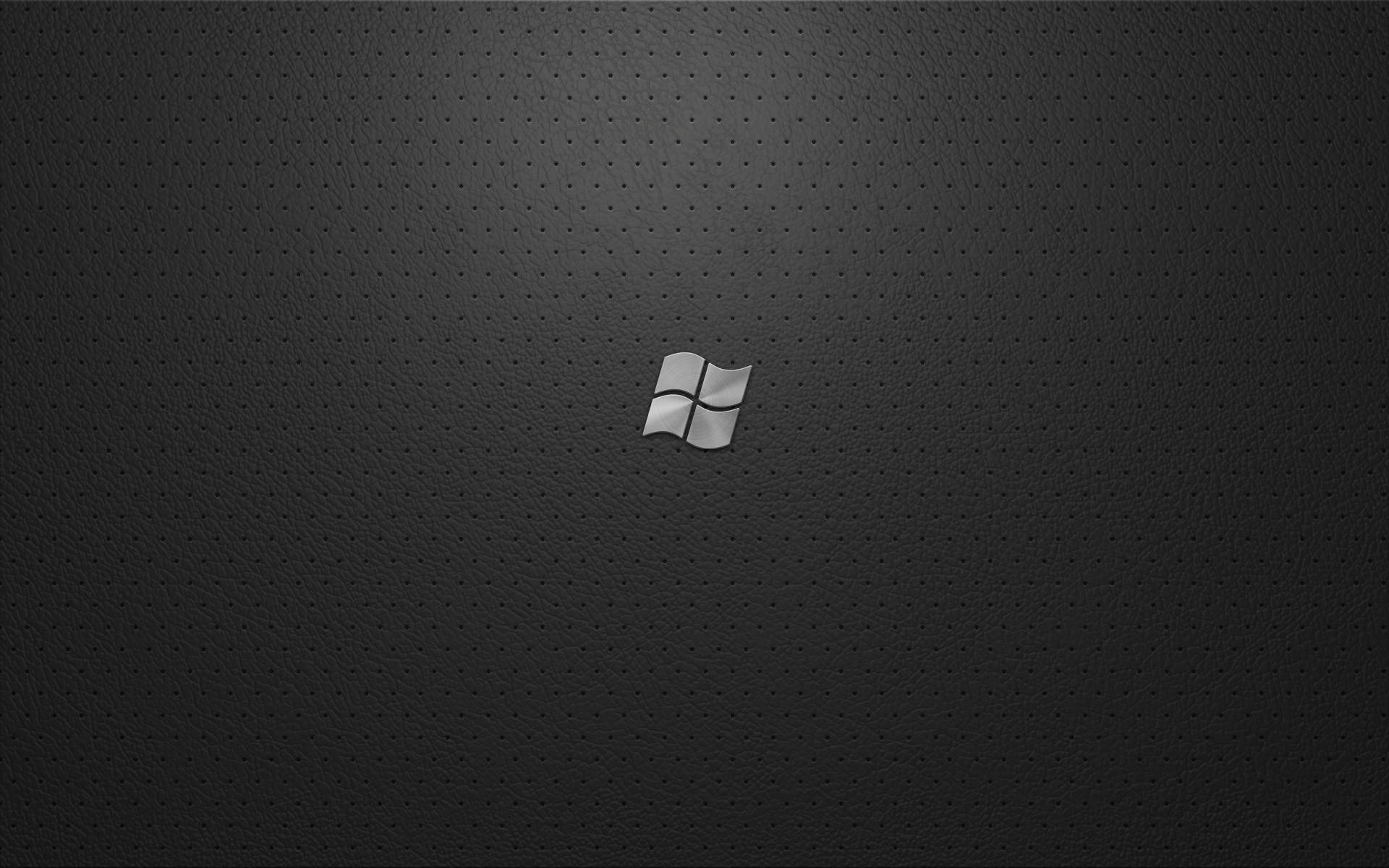 Windows 桌布 壁紙 — 一個時尚的銀色Windows標誌居中在深色穿孔皮革狀表面上，帶有柔和漸變照明。