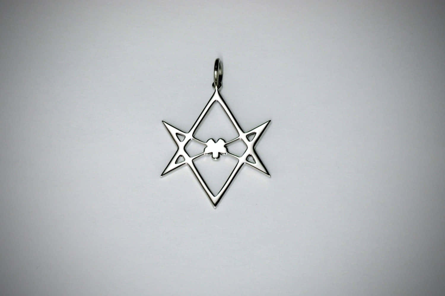 Thelema 桌布 壁紙 — 一個時尚的銀色共濟會吊墜，帶有星形和方形設計，中央有指南針，在純淺灰色背景上拍攝。