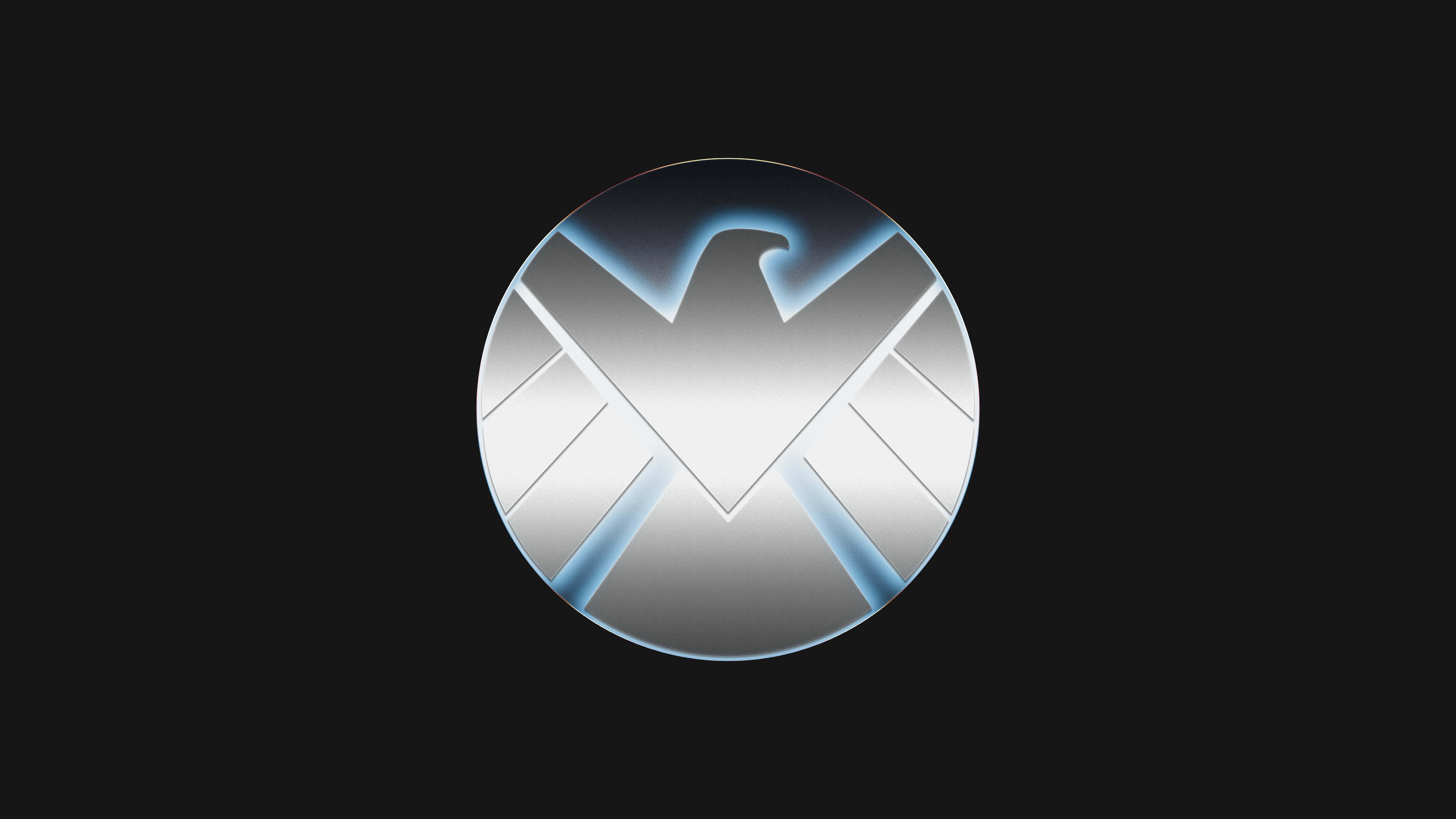 shield 桌布 壁紙 — 一個時尚的銀色圓形徽章，中央有風格化的鷹和發光的藍色點綴，位於黑色背景上。