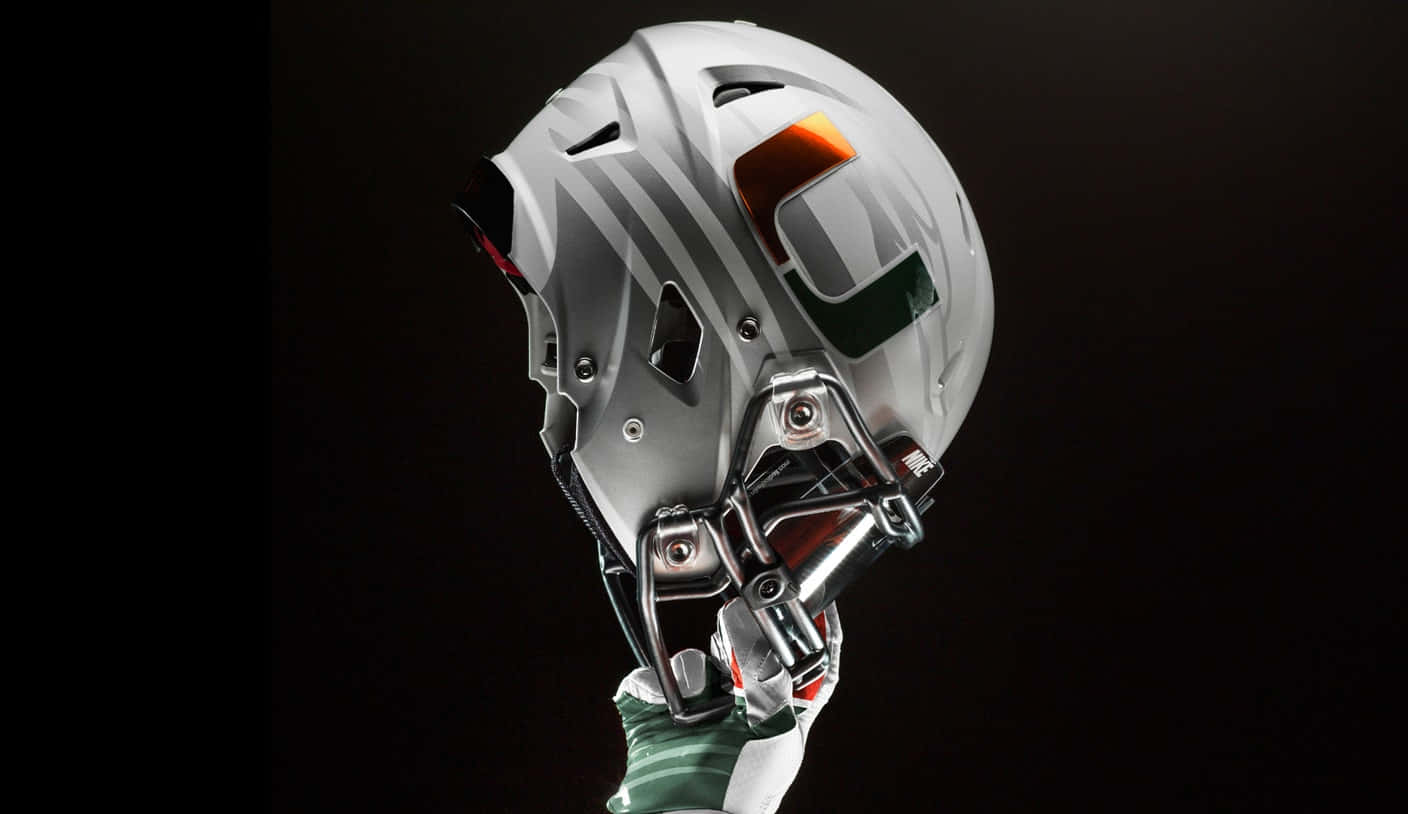 Miami Hurricanes 桌布 壁紙 — 一個時尚的銀色美式足球頭盔，帶有橙色和綠色的「U」標誌，置於黑色背景前。