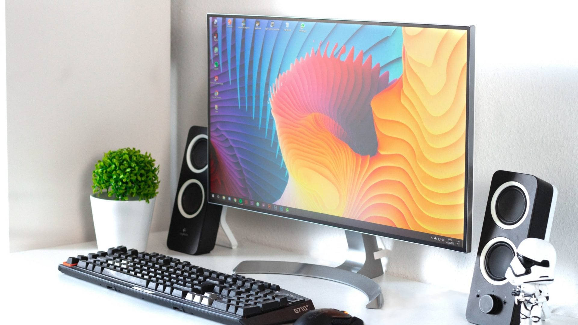 Desk 桌布 壁紙 — 一個時尚的電腦設置，顯示器上帶有充滿活力的抽象桌布，兩側是揚聲器和一個小盆栽植物。